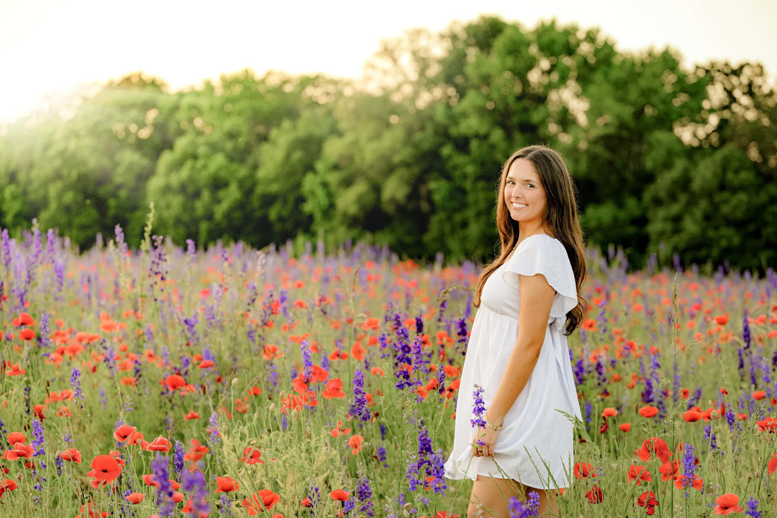 senior stands in white dress in a monroe wildflower field