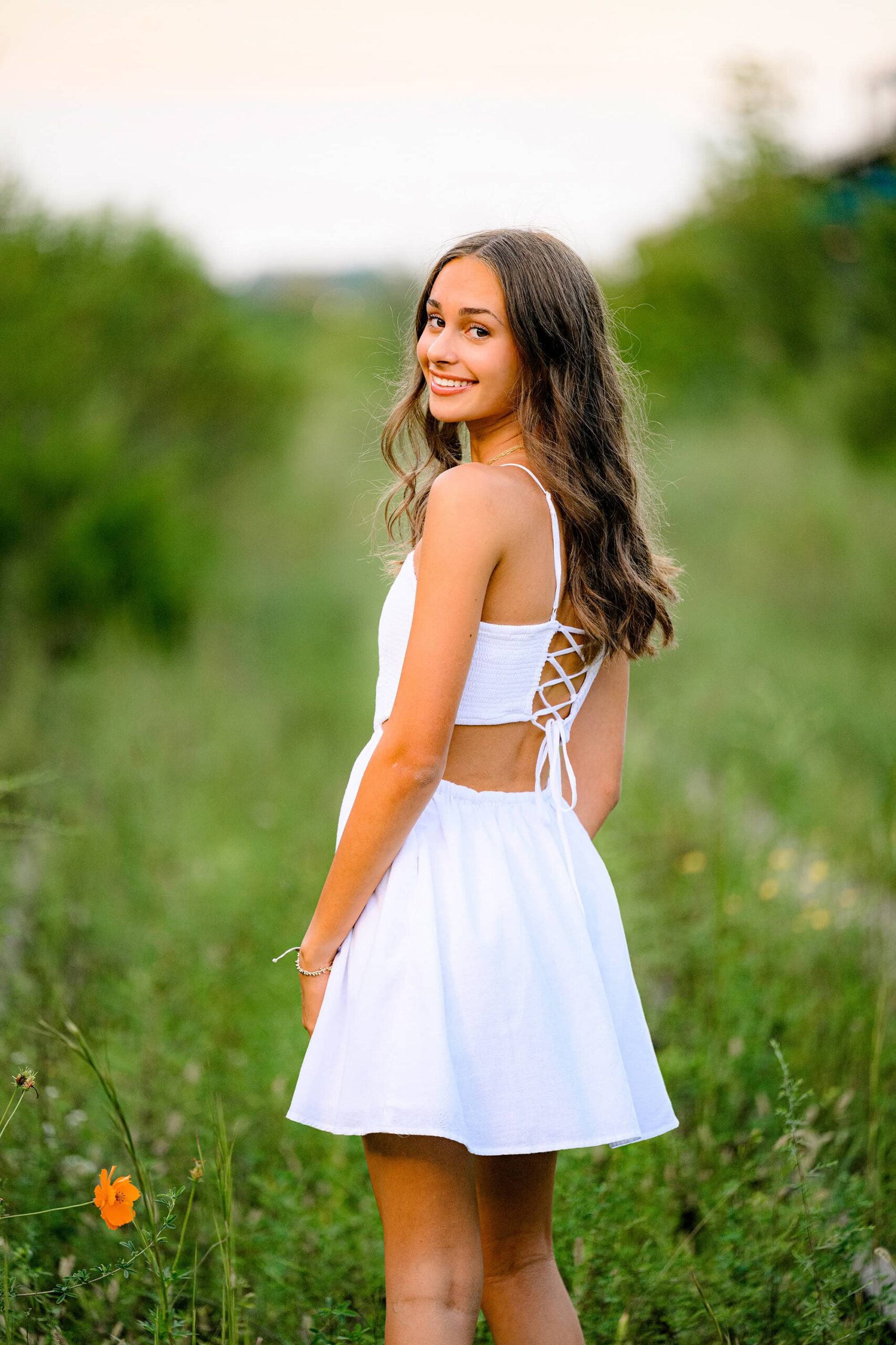 charlotte senior looks back over her shouder while wearing a white dress with a lace up back
