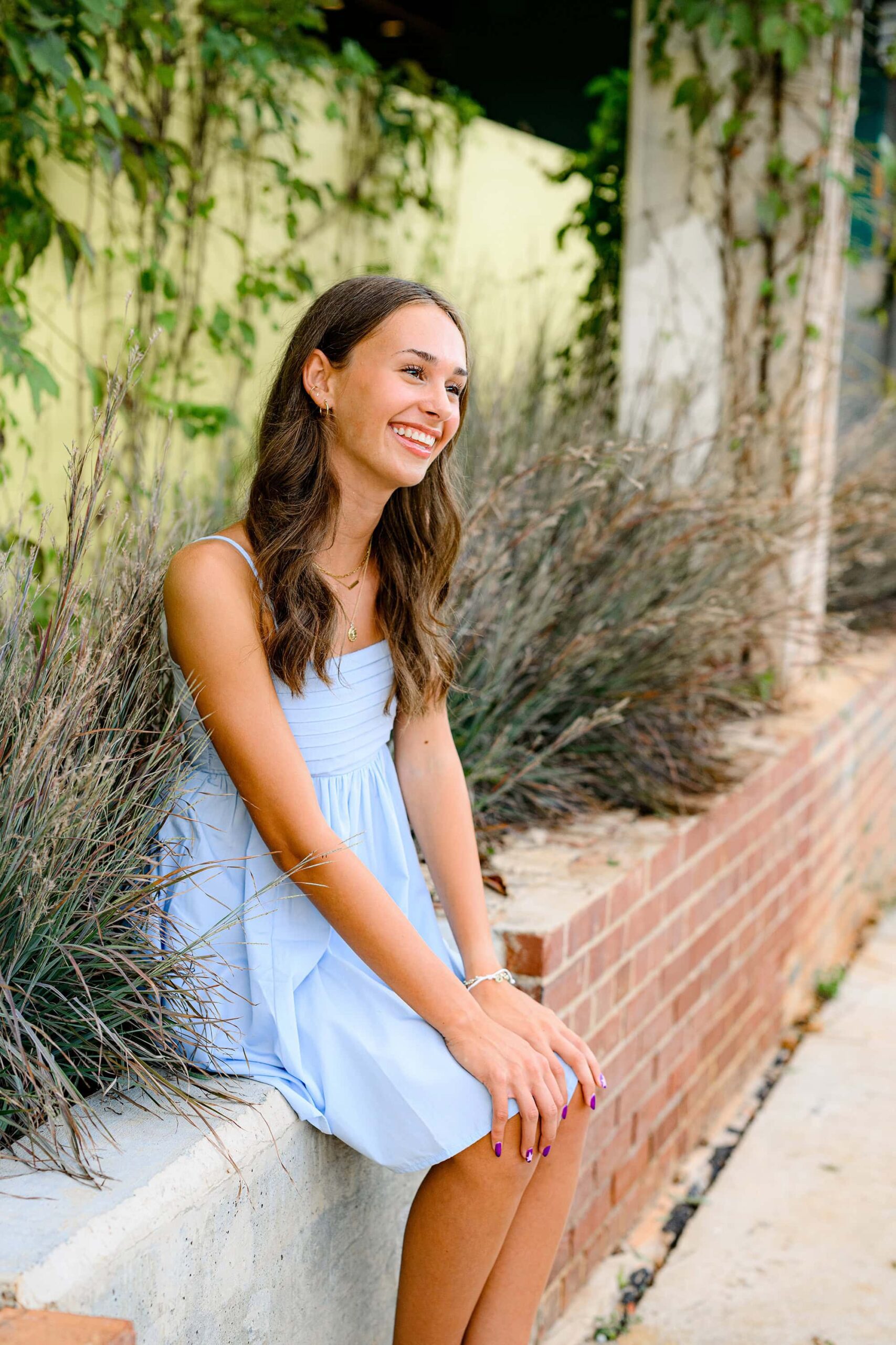 senior smiles as she looks off camera sitting on a wall at camp north end