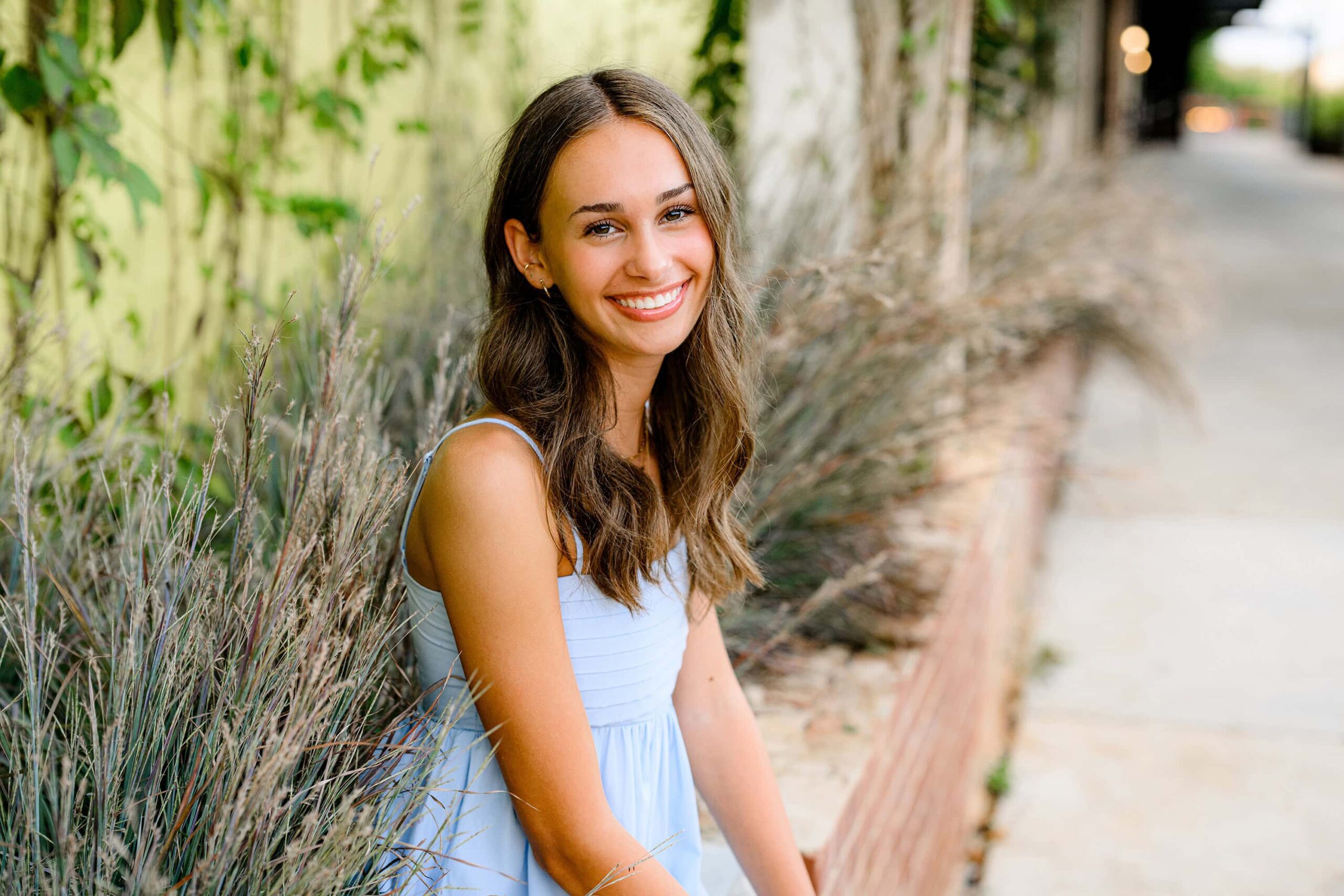 sweet senior smile on this dark hair ardrey kell graduate wearing a blue dress and sitting on a brick ledge