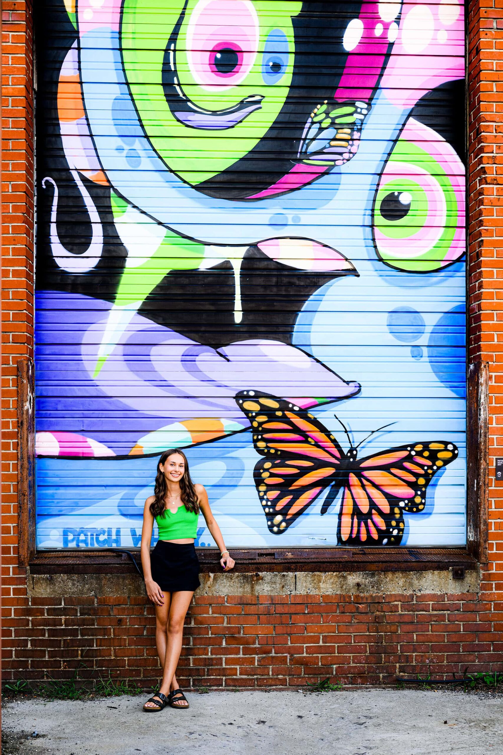 charlotte senior poses in black skirt and green top in front of a graffiti wall at camp north end in uptown