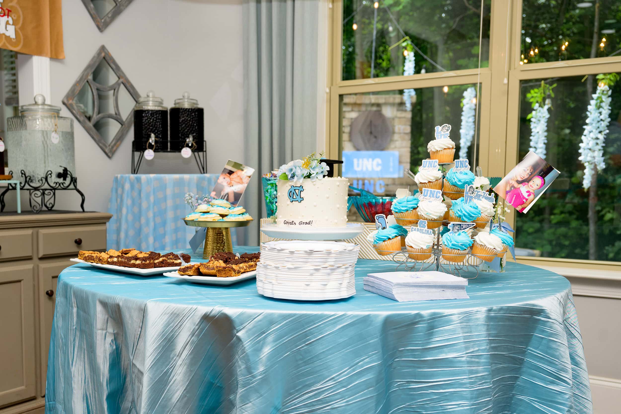 dessert table at high school graduation party with blue iced cup cakes, brownies, cookies, and a large graduation cake