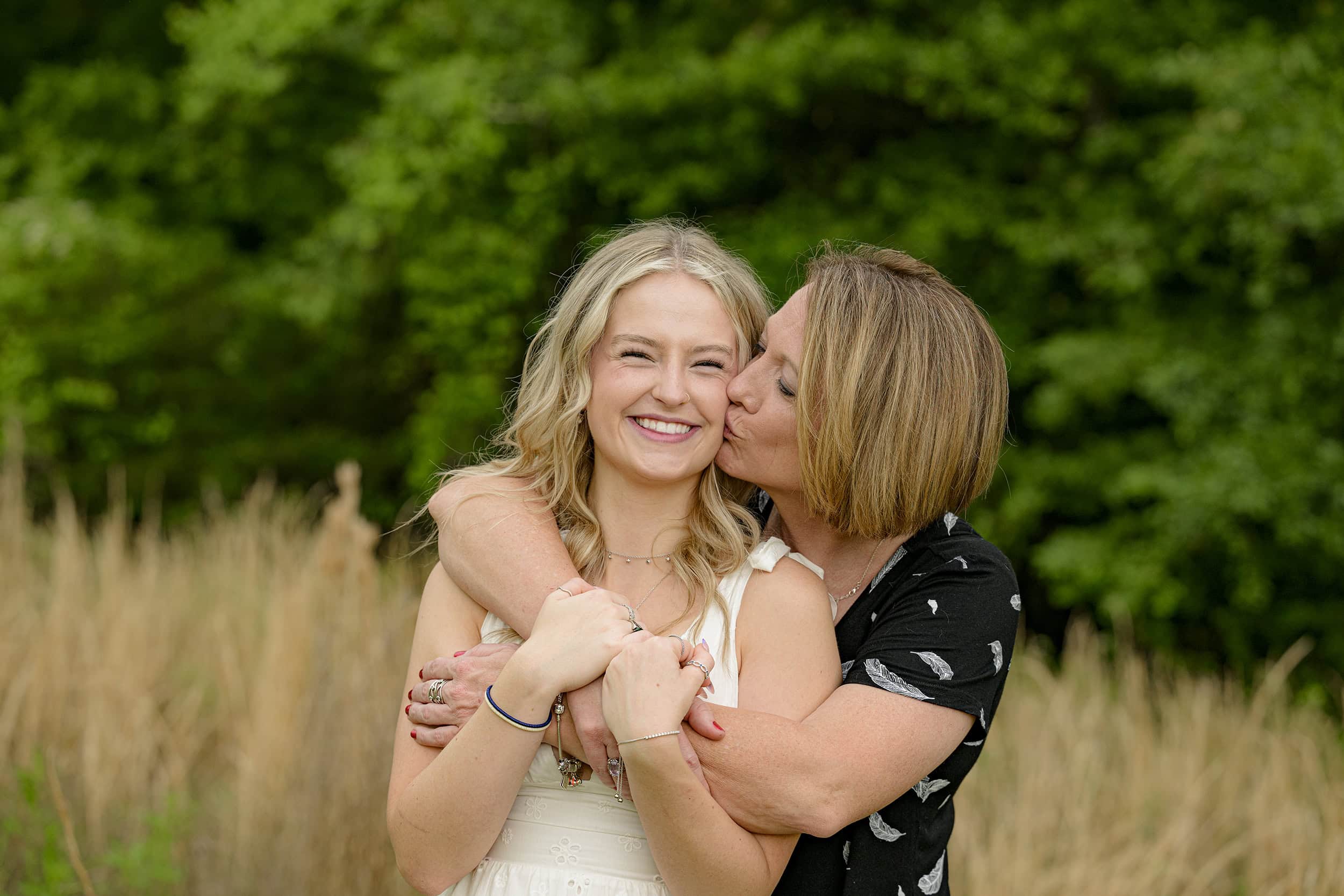 senior mom hugs and gives graduate a kiss on her cheek during her senior photo session