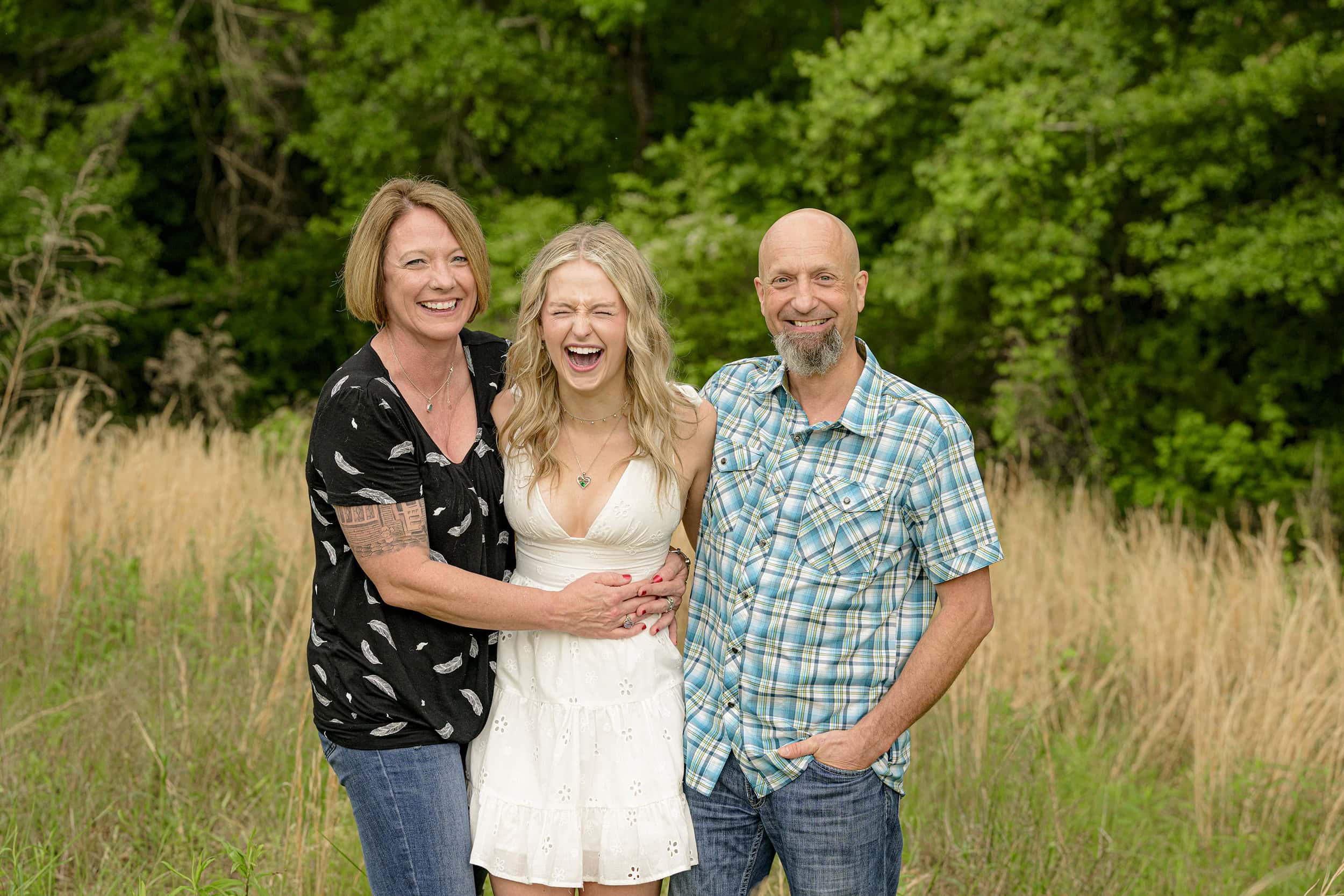laughing grad stands out between parents during their family photos before her senior portrait session