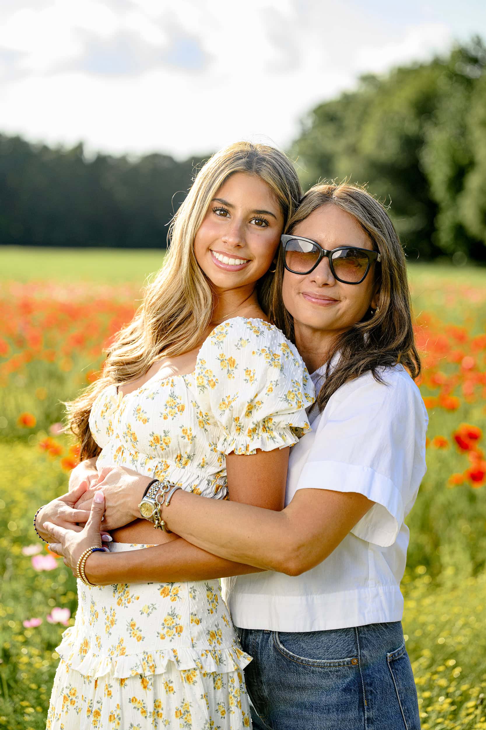 mom and charlotte teen hug in a flower field filled with red poppies during senior's portrait session