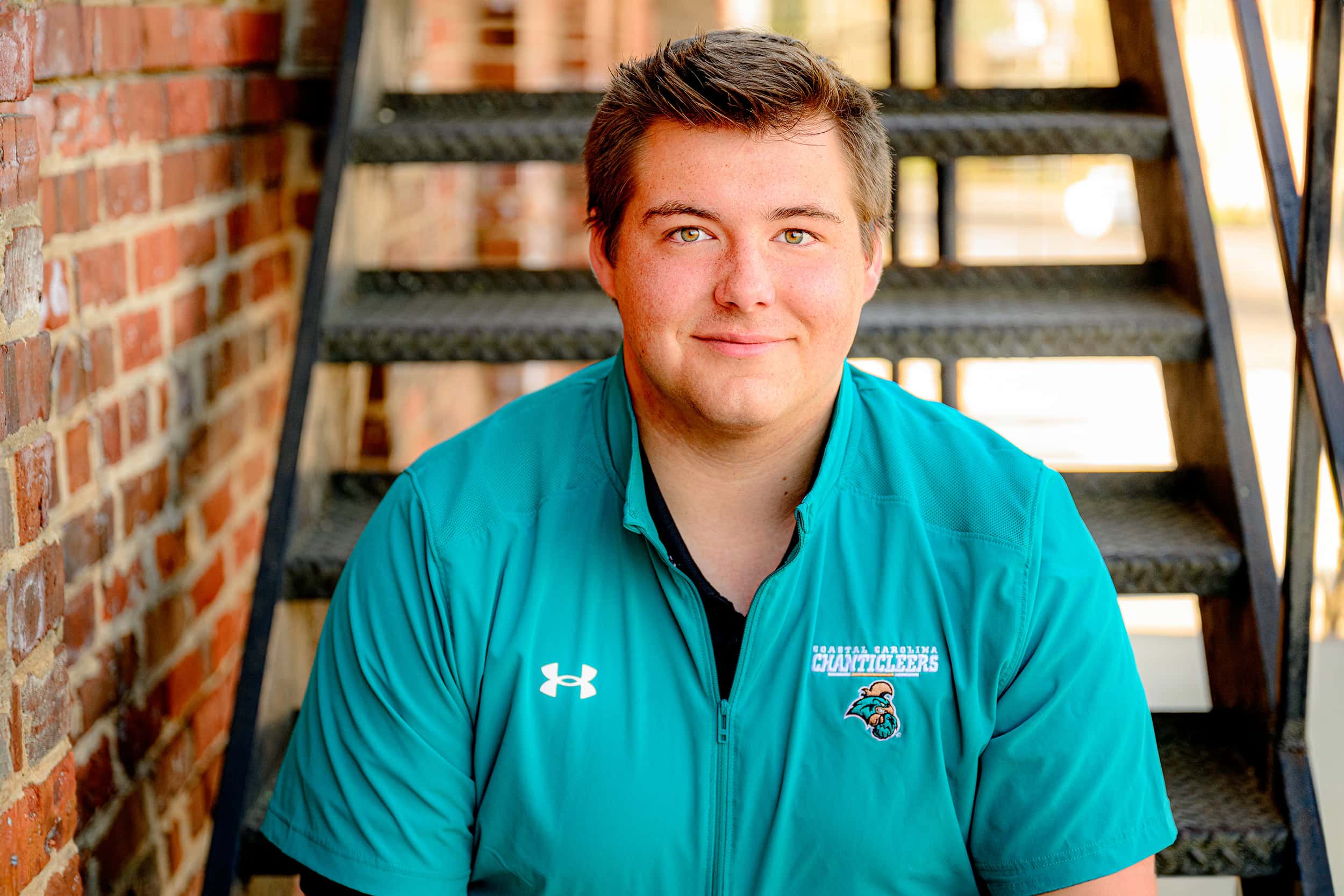 CHS graduate sitting on metal staircase wearing a coastal carolina shirt for his senior photos