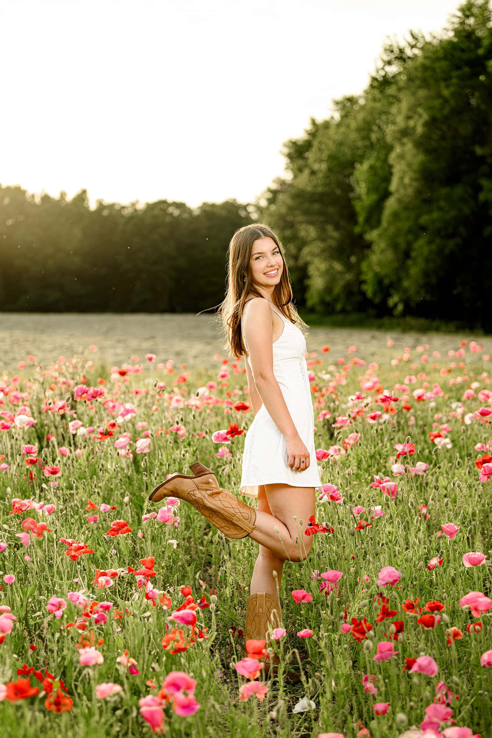 Charlotte Senior Photo of dark hair grad standing in the flower garden at Blue Hill in Monroe wearing a white dress and boots for her graduation photos for her wildflower themed party