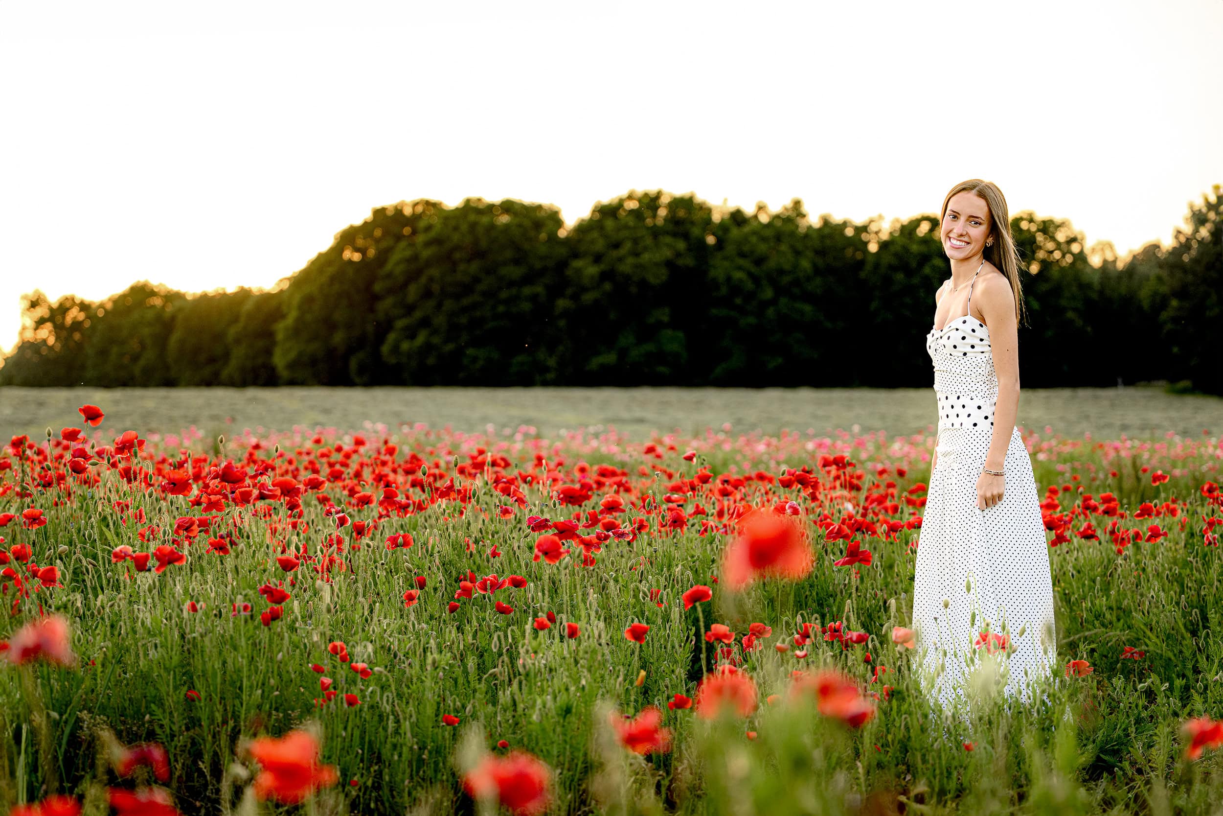 Charlotte senior standing in a red poppy field for her graduation photos wearing a black and white dress