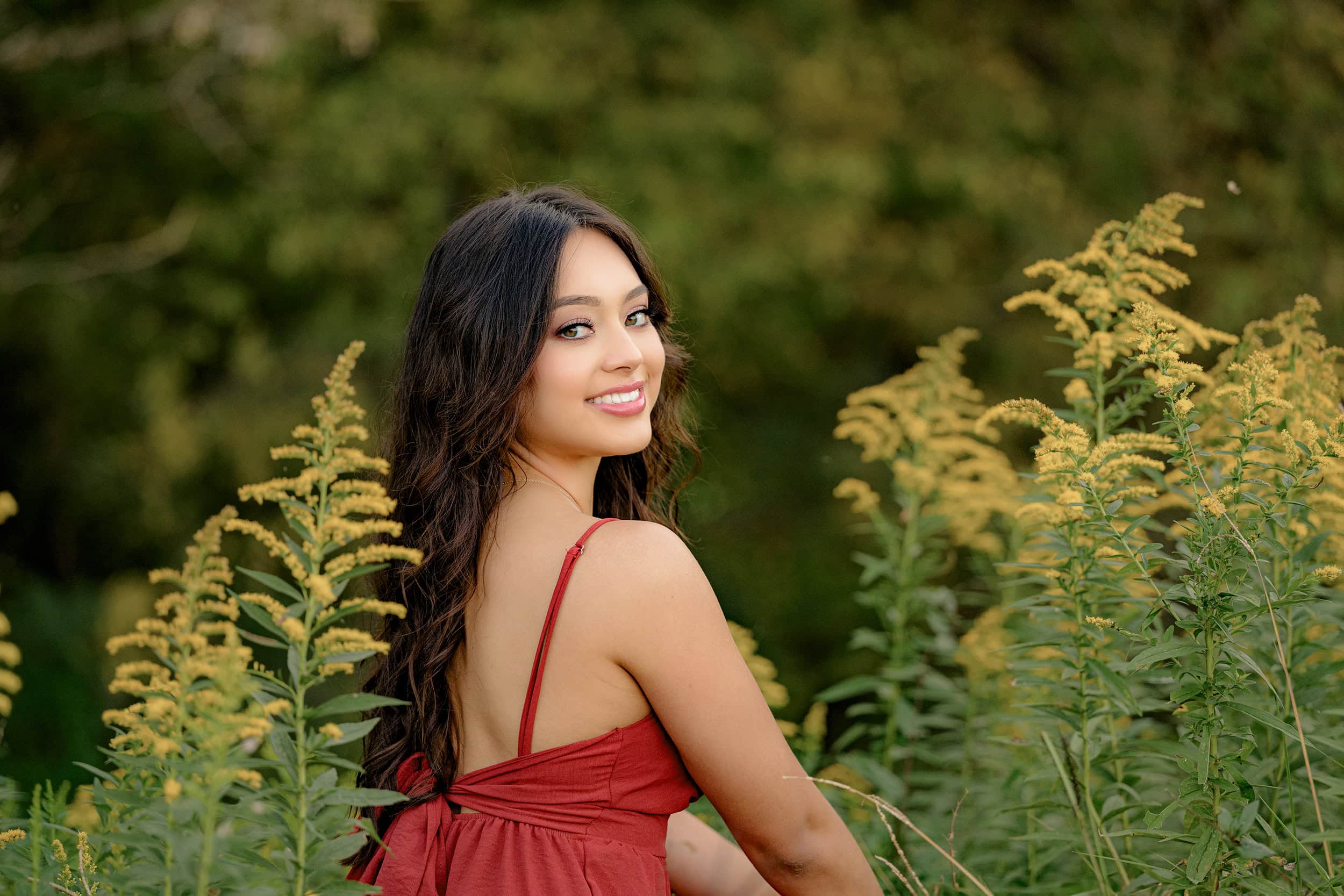dark hair cuthbertson high school grad wearing red stands out against the green and yellow tons of fall during her senior portraits