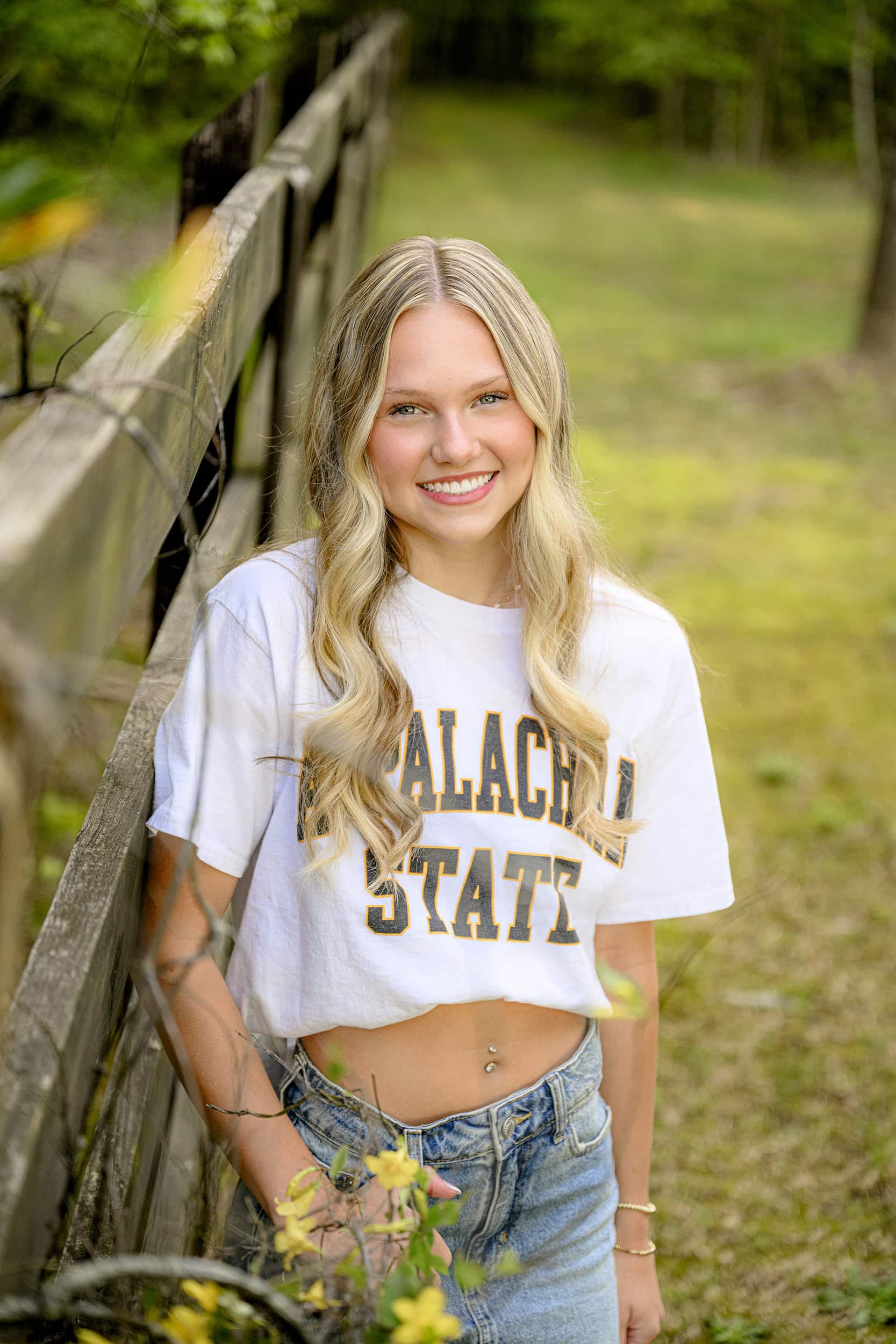 yellow spring blooms help highlight this blonde parkwood highschool senior wearing her college app state t shirt during her senior photos in a waxhaw park