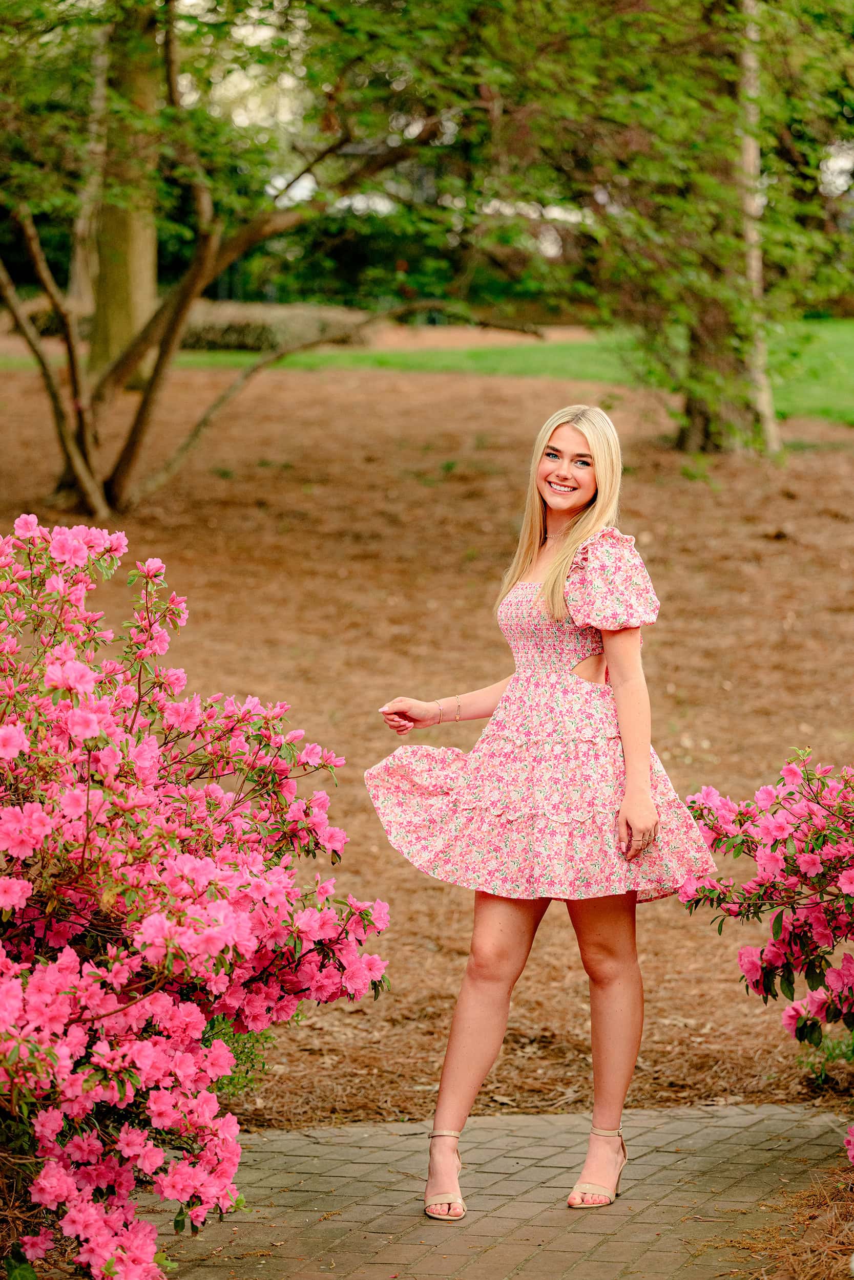 blonde cuthbertson high school senior twirls in her pink floral dress in early spring surrounded by bright pink azelea blooms in rock hill sc park