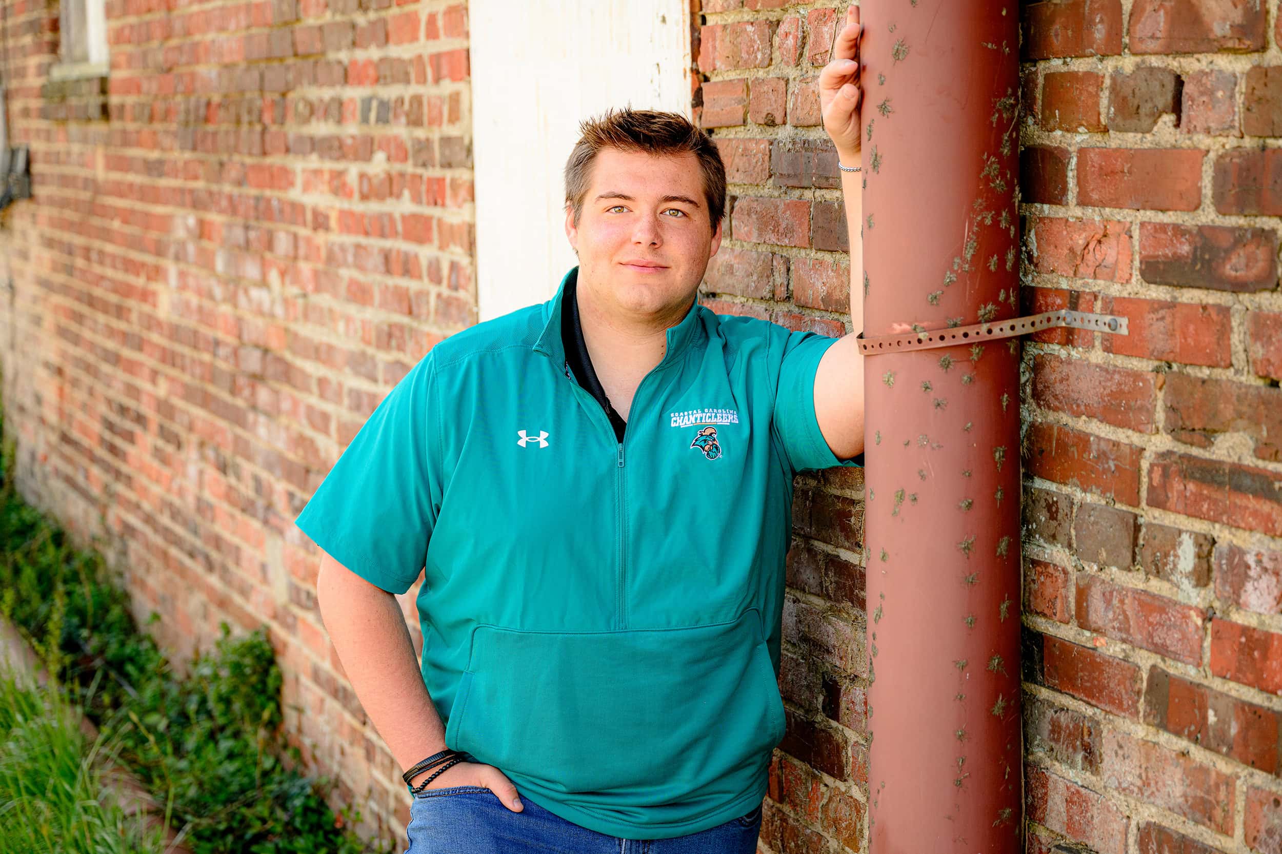 cuthbertson high school football player wears Coastal Carolina shirt as he leans against a brick wall and pipe in waxhaw nc