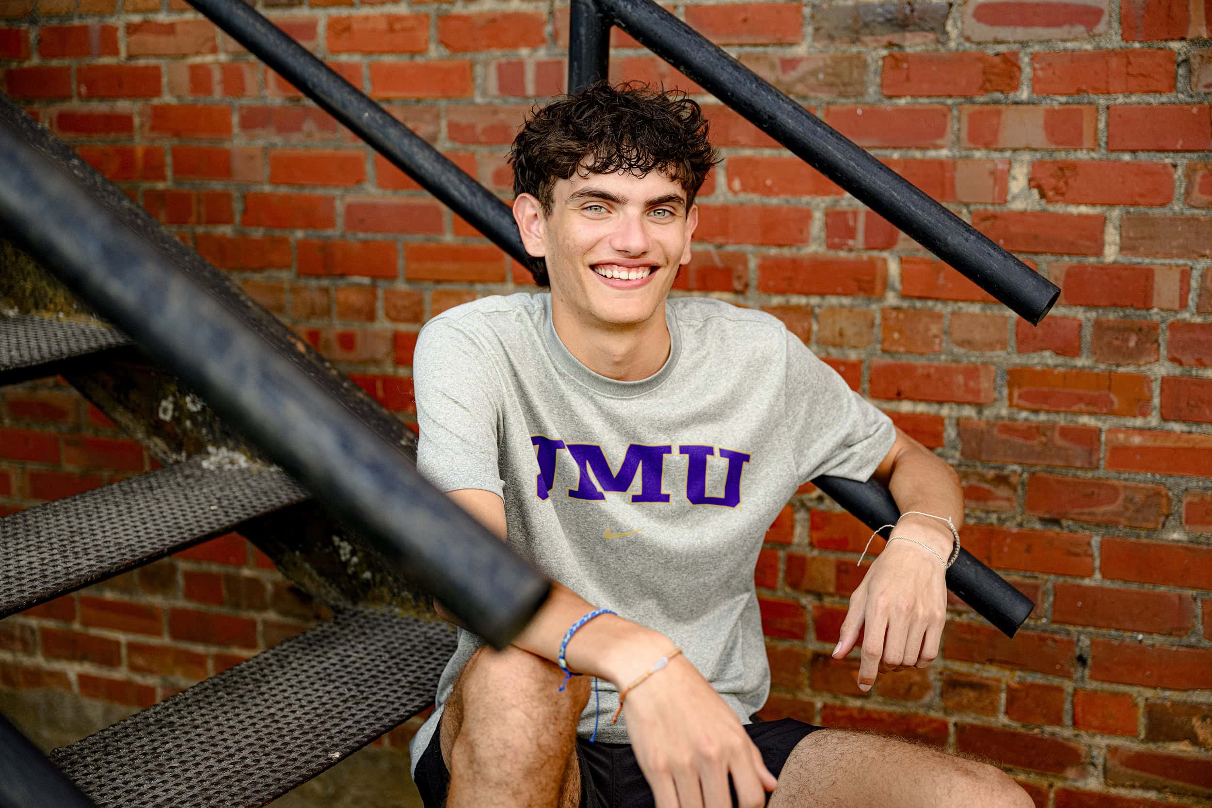 Cuthbertson high school senior boy sits on urban staircase wearing future college James Madison University T shirt smiling with excitement