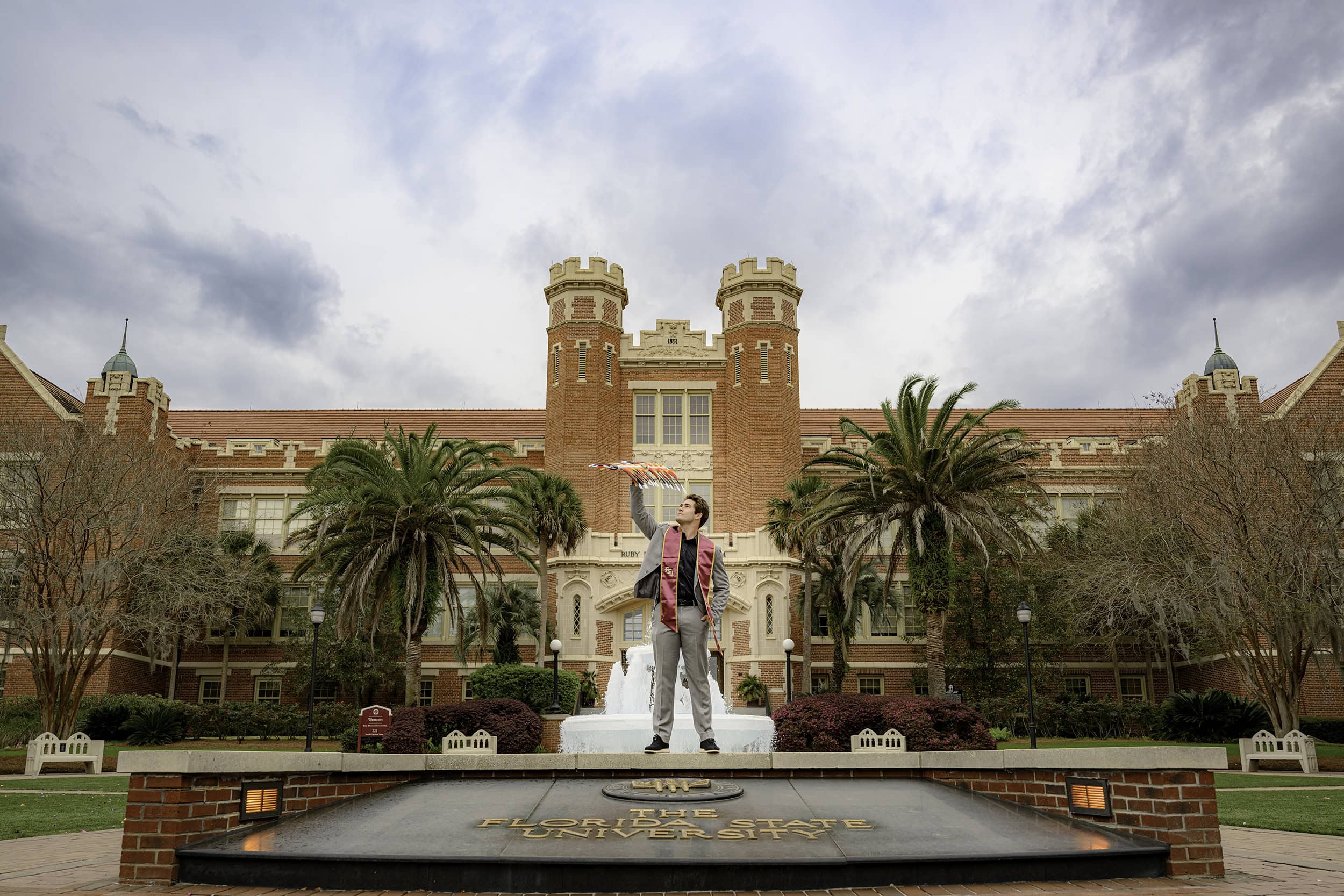 Florida State University Wescott Fountain is background for this college senior holding a FSU spear and wearing his stole and grey suit