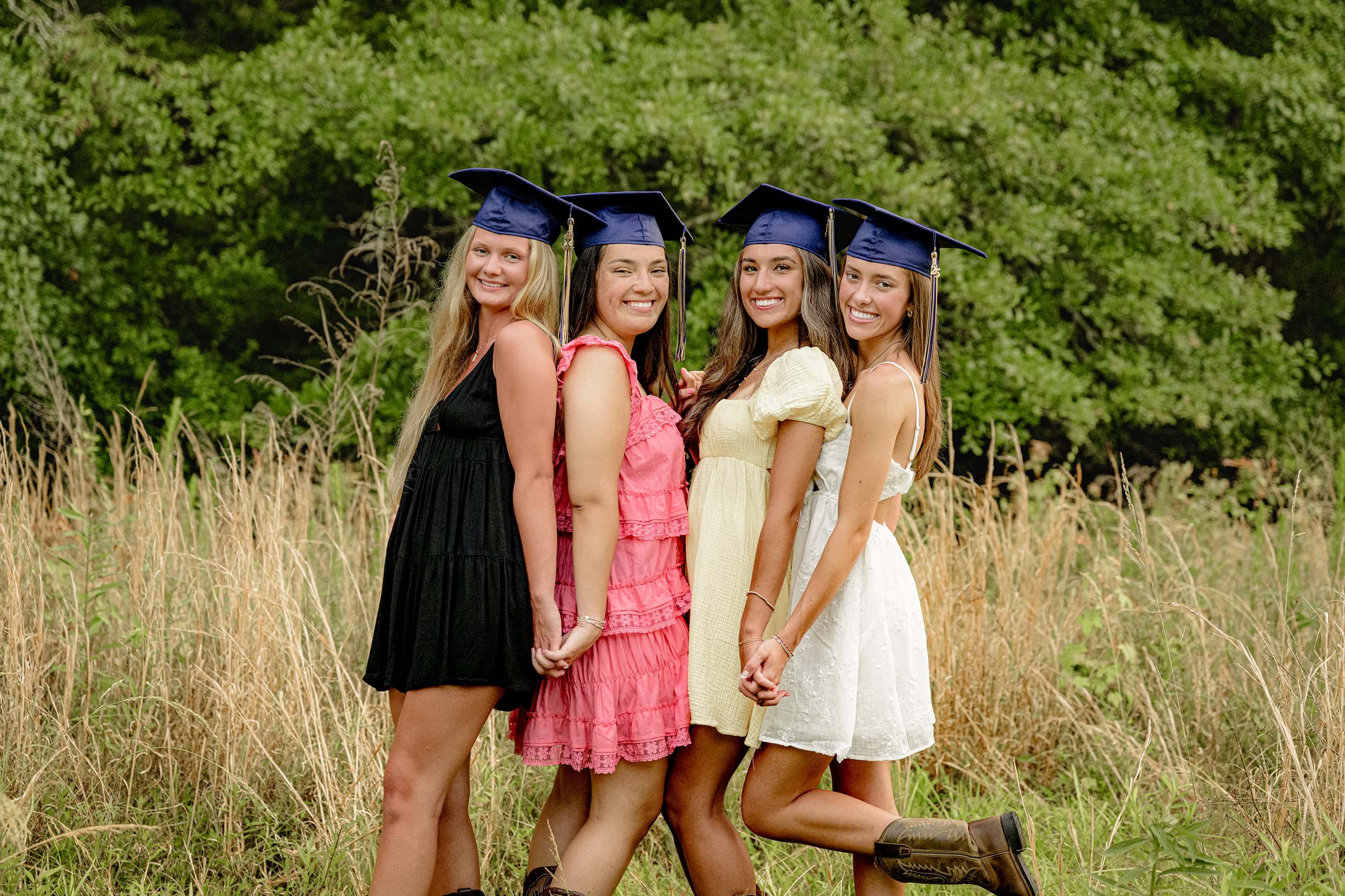 four besties wearing colorful sundresses and cuthbertson high school graduation caps stand together in a charlotte field