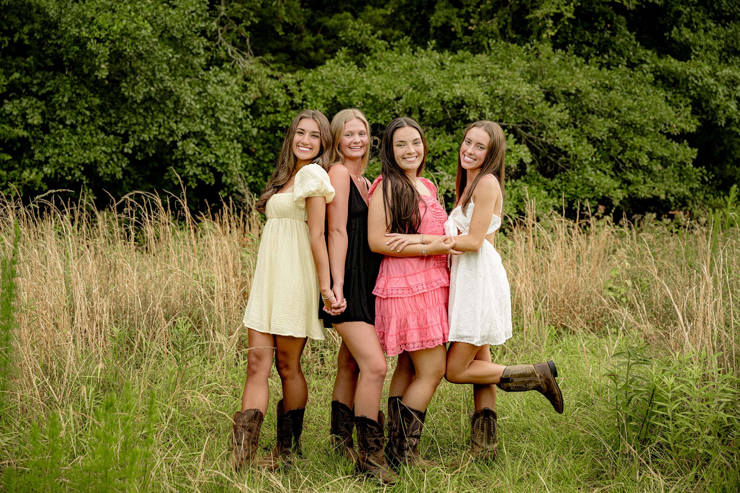 Four Charlotte Senior Bestie Girls standing in sundresses in a field wearing boots