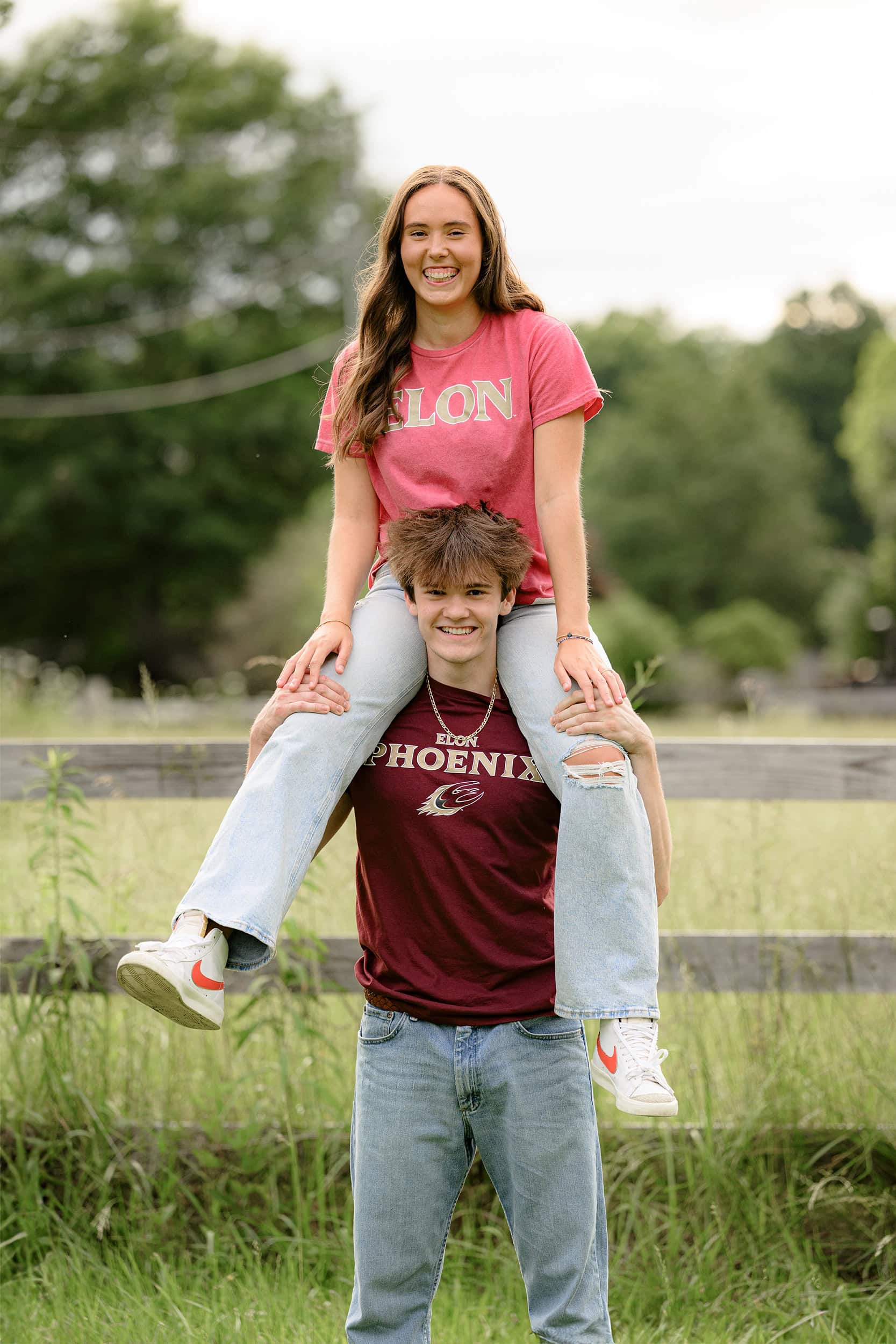 Charlotte sister sitting on her twin brothers shoulders during their twin bestie session in a field with a fenceline behind them