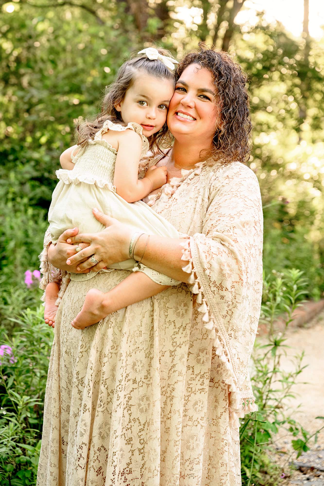 mom and daughter posed together with daughter sitting on moms expectant belly both dressed in cream