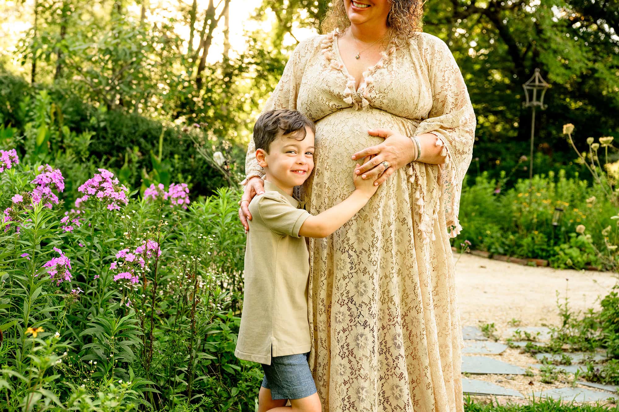 big brother cradles his mom's pregnant belly during their outdoor maternity session in a charlotte flower garden