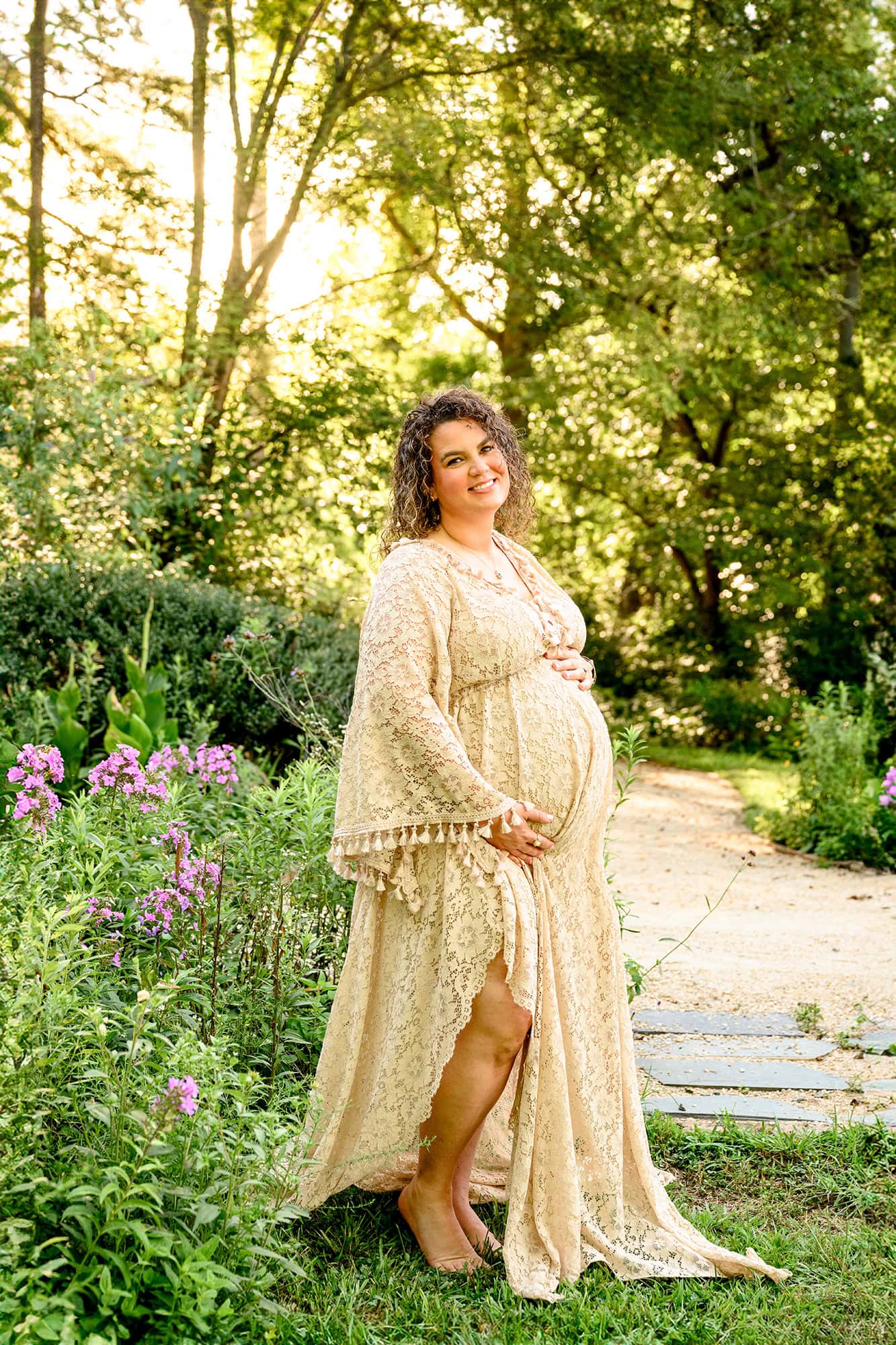 pregnant mom stands in a boho styled maternity dress in a natural flower garden area