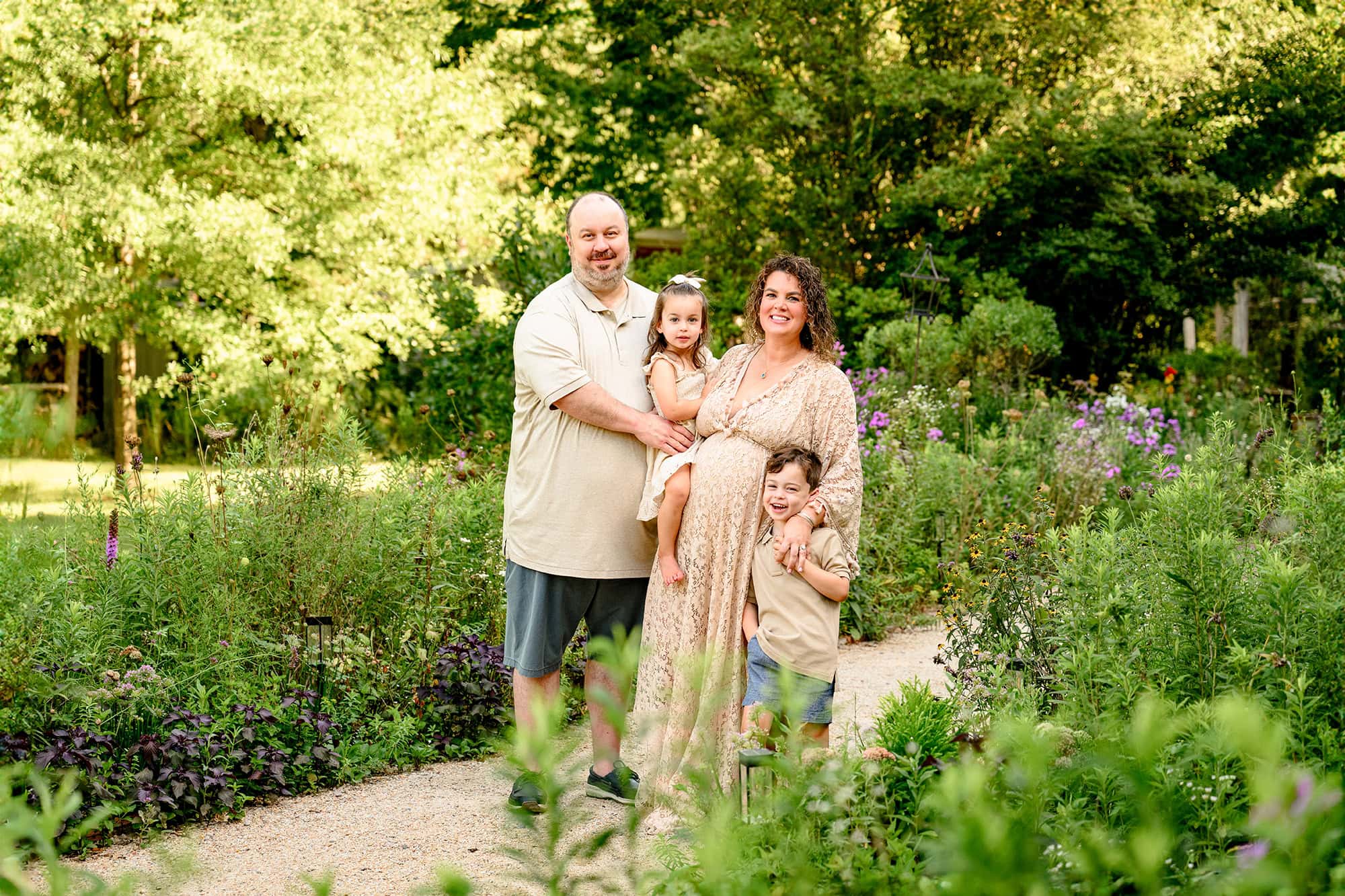 charlotte area family of 4 expecting their 3rd child standing together dressed in natural colors in a flower garden