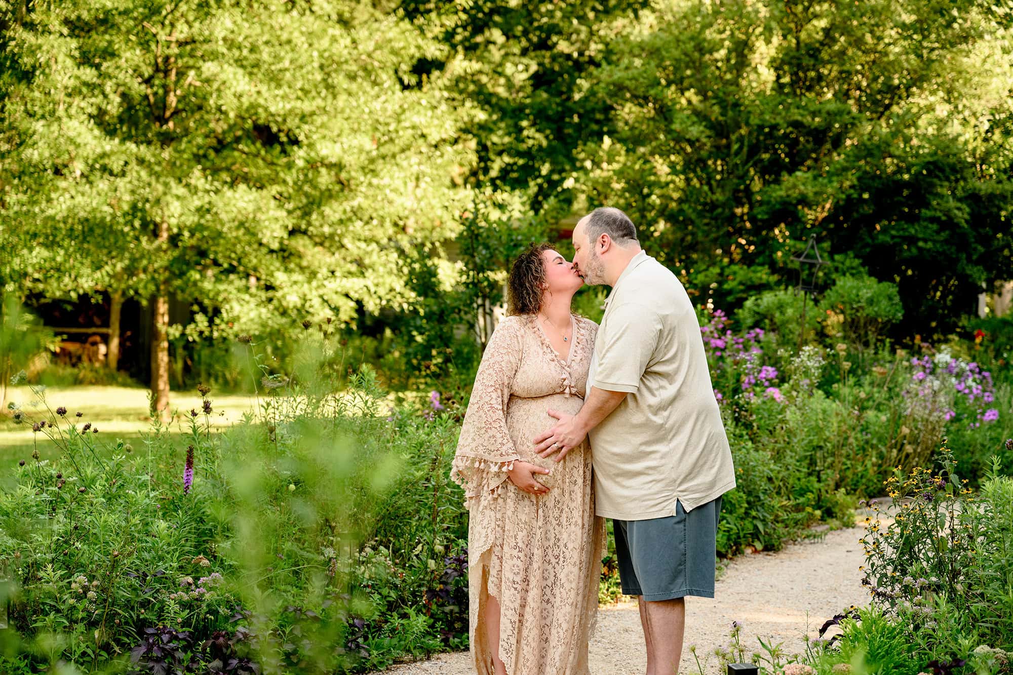 husband and wife expecting their third child celebrate their last baby with a maternity session and a kiss in a charlotte area flower garden