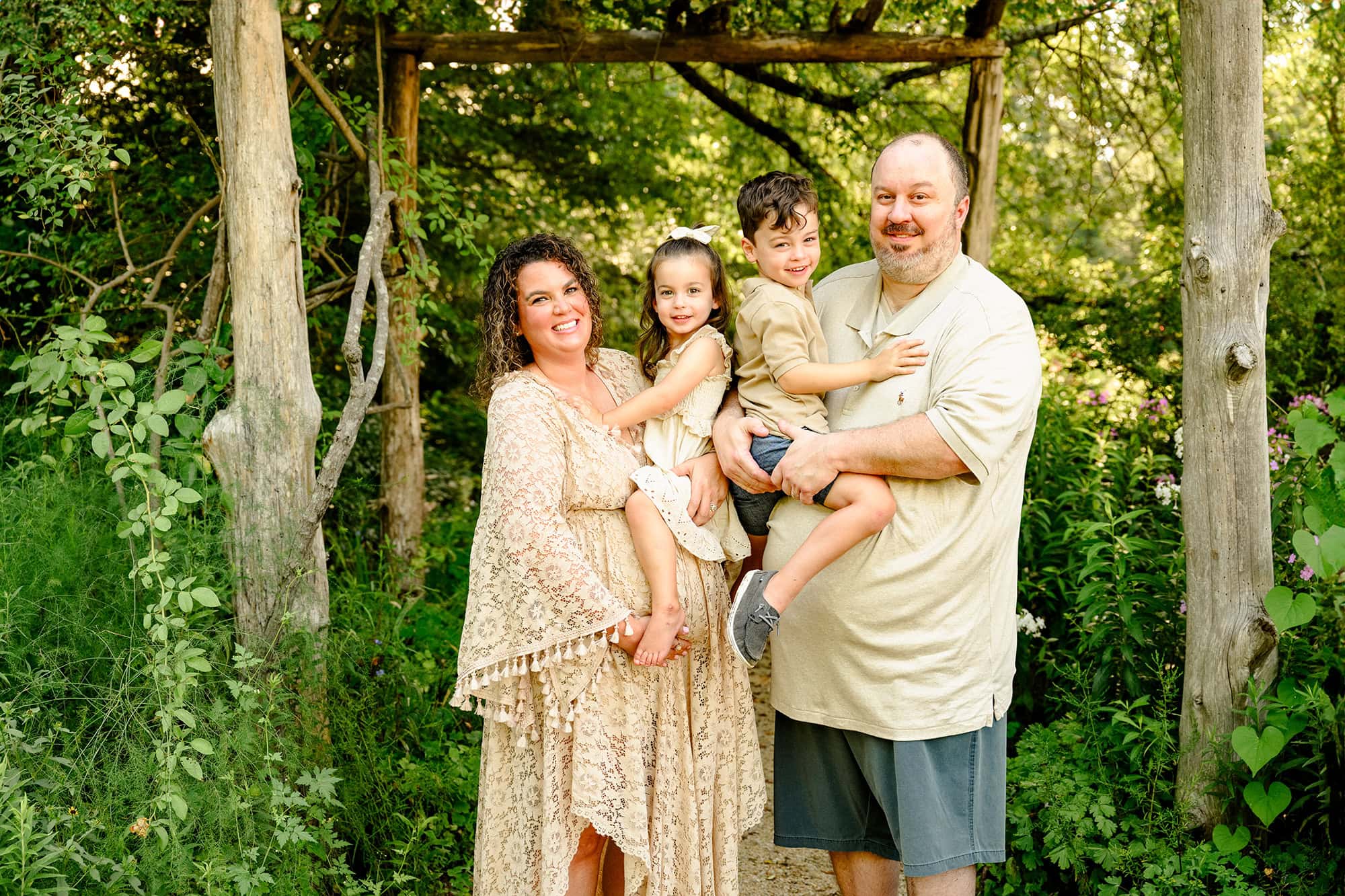 photo of mom and dad holding their kids in an outdoor maternity session in a flower garden in morning light