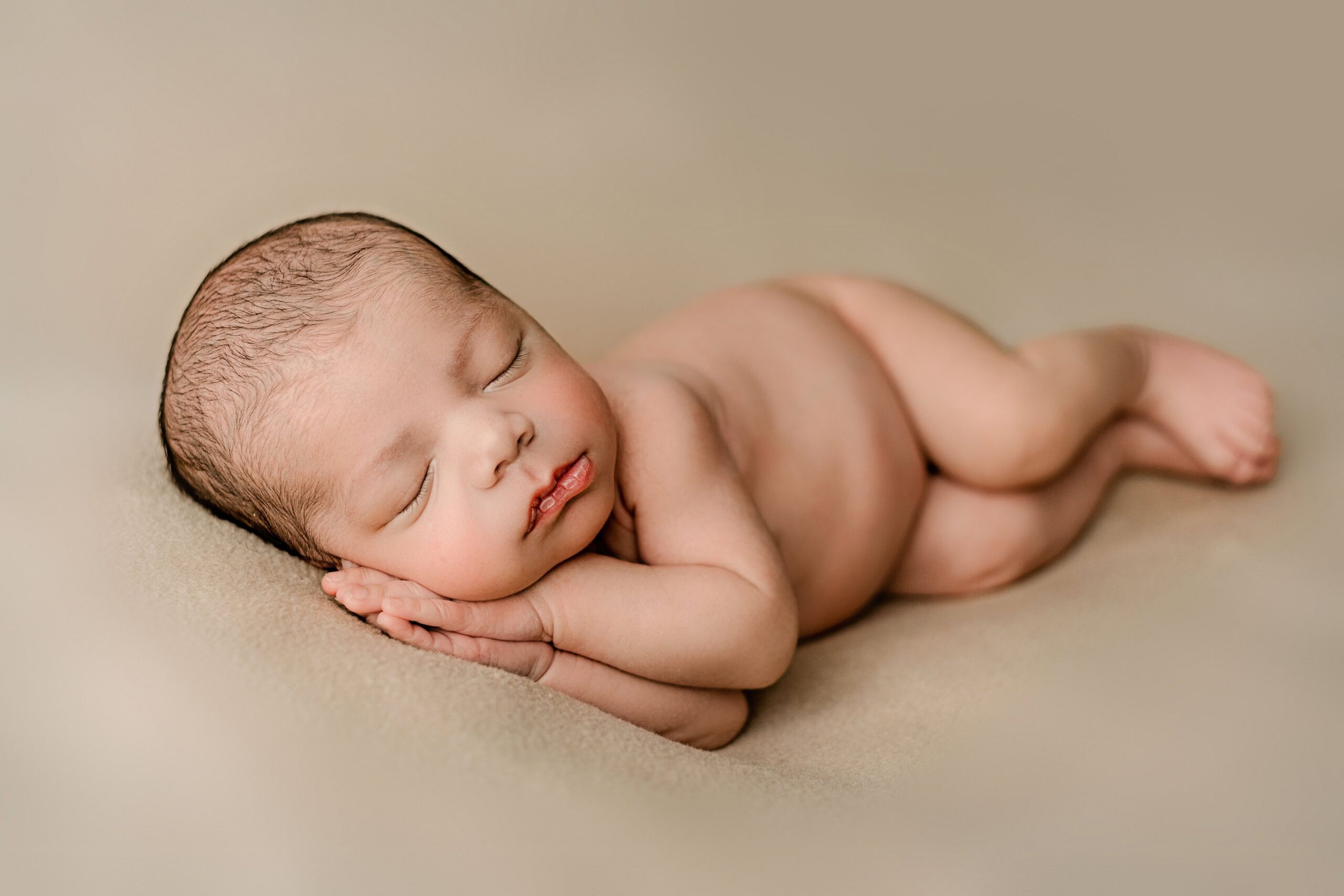 little newborn baby boy lays on his side with his hands under his cheek resting peacefully after birth