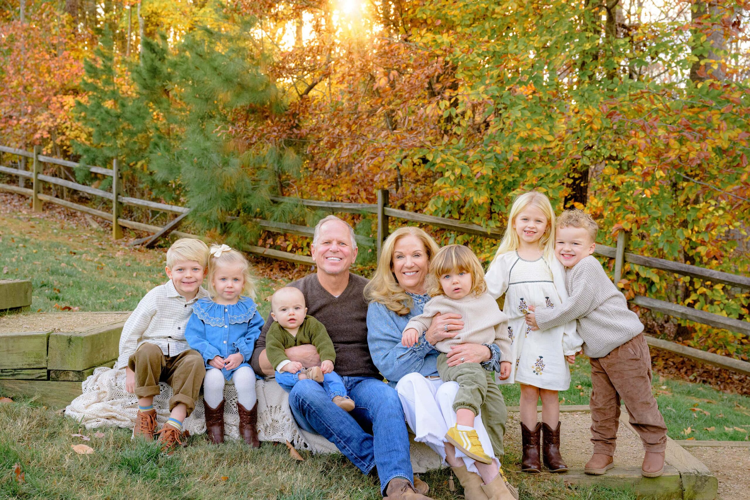 grandparents sit in a waxhaw area park with their grandchildren all around them surrounded by fall colored leaves