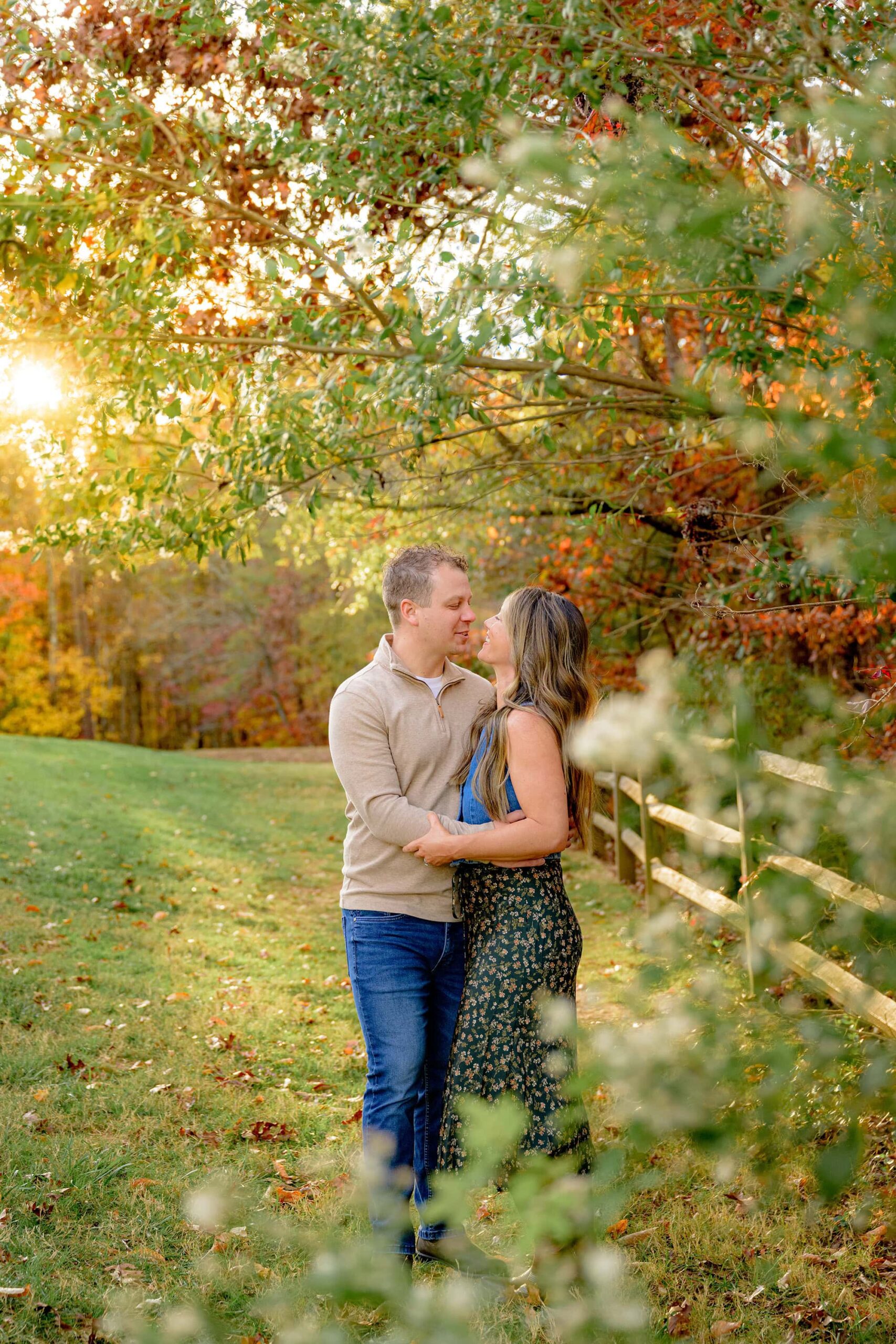 husband dressed in a brown sweater and jeans looks at wife dressed in denim and floral skirt in a fall location perfect for autumn portraits