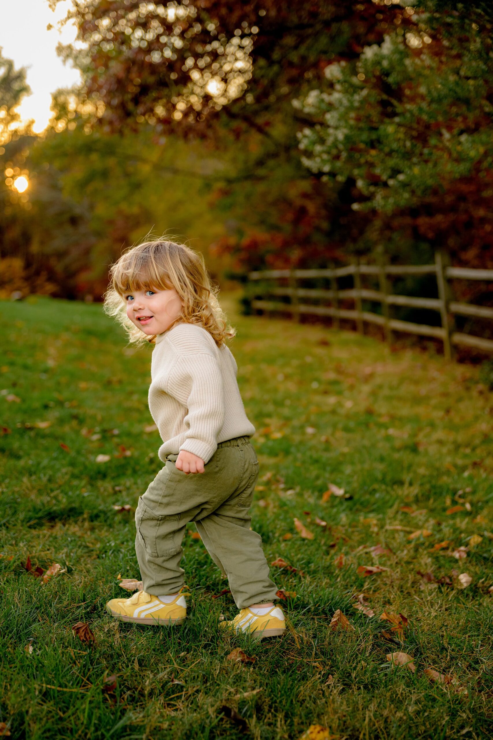 little charlotte area boy dressed in a cream sweater and pants runs in waxhaw park looking back over his shoulder