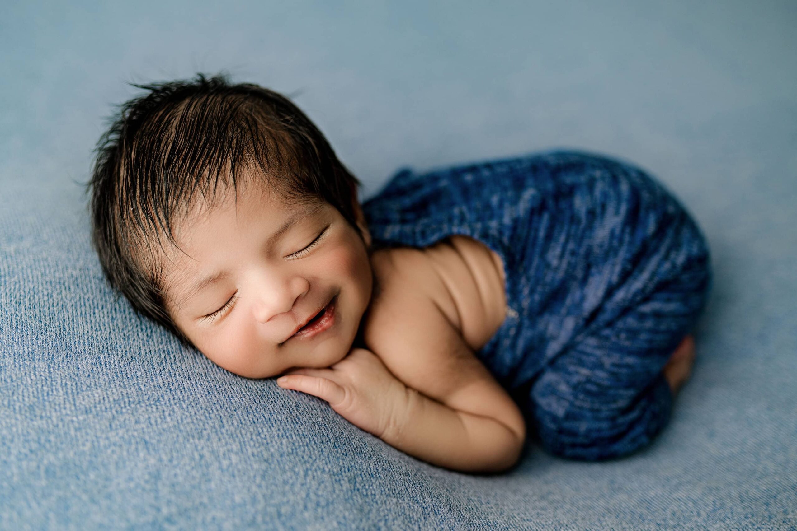 little newborn boy lays on his belly smiling on a blue studio background for his charlotte newborn photos