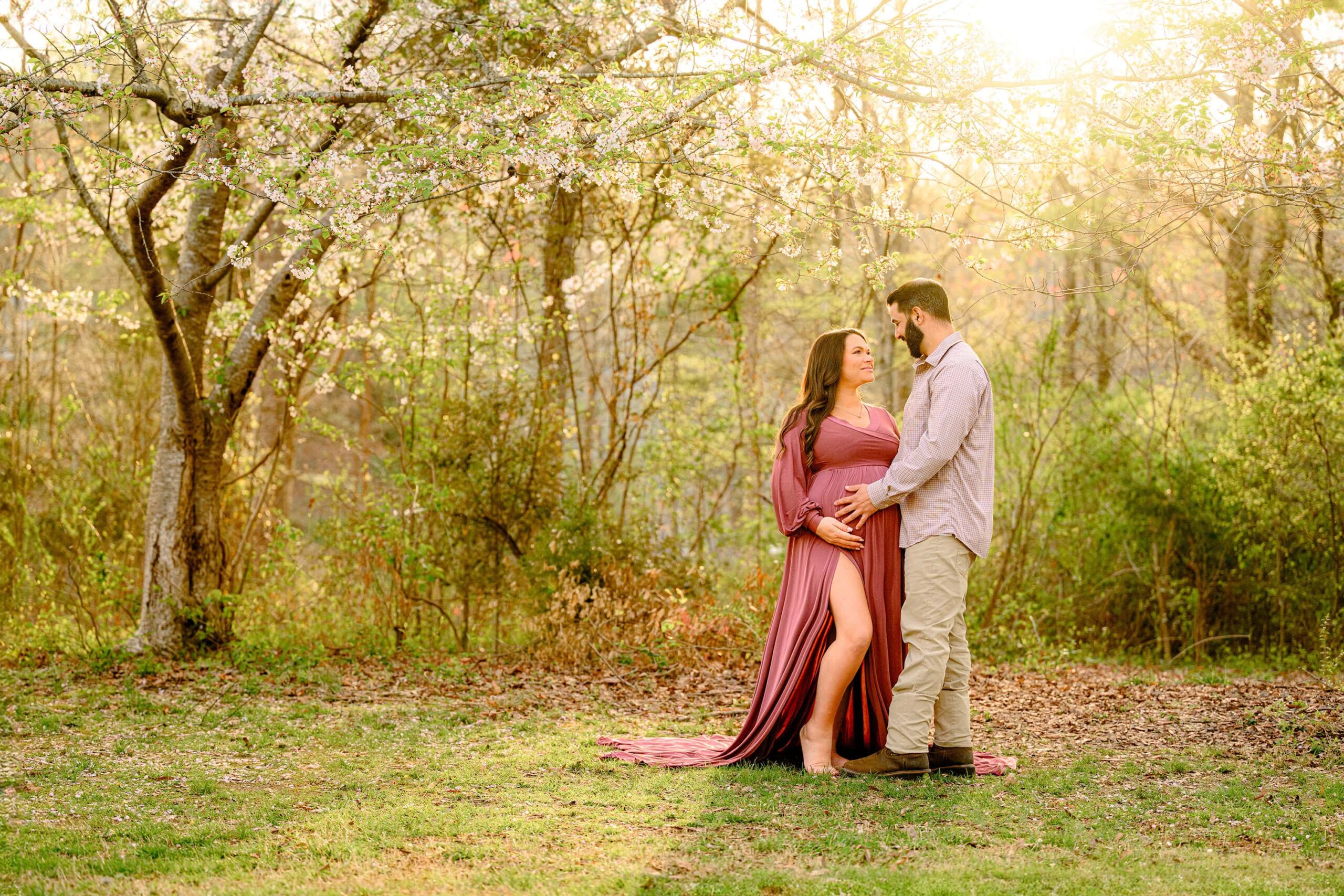 Charlotte couple standing in a waxhaw park location during maternity photos with mom wearing a pink dress and dad wearing a button down and khakis 
