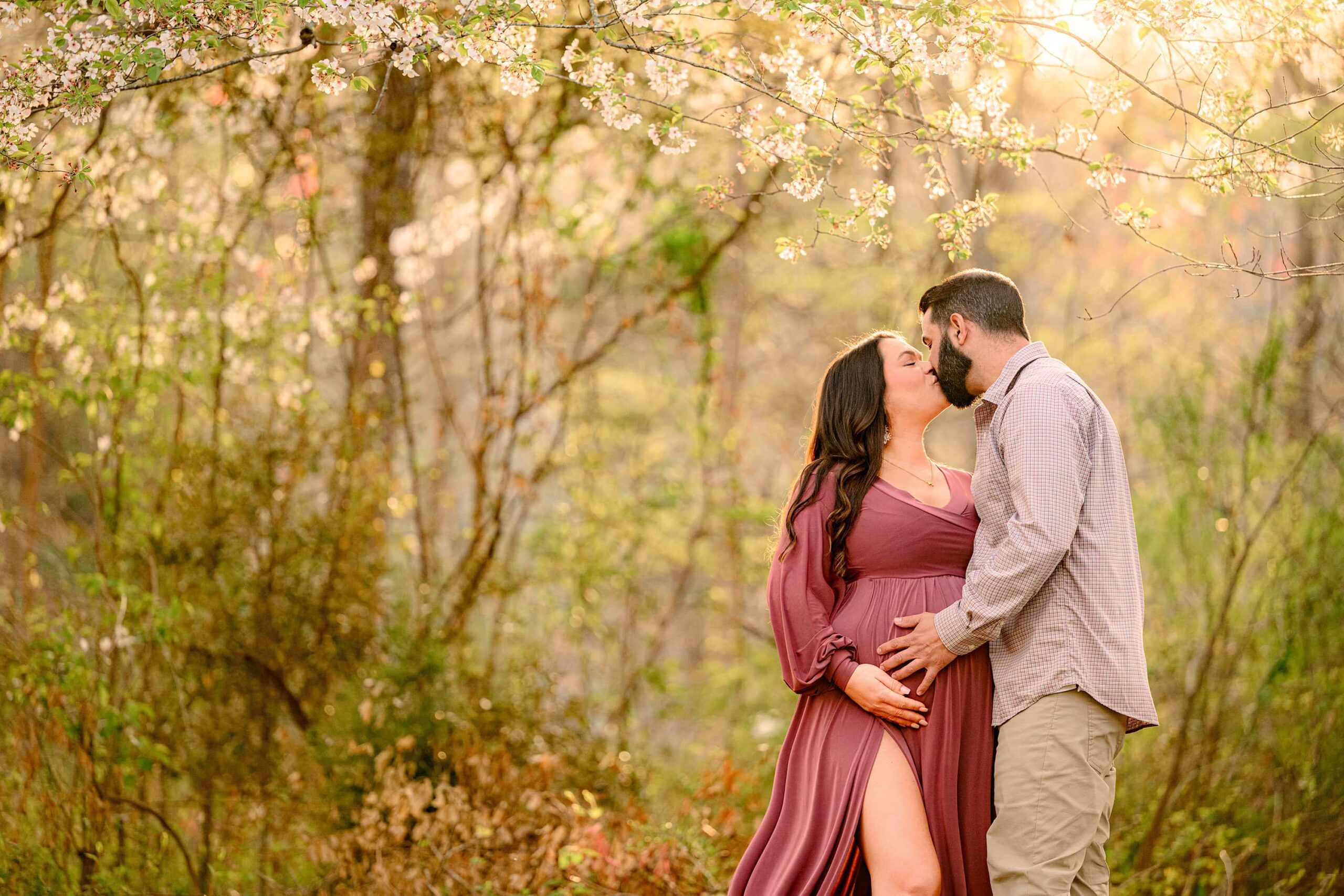 Charlotte expecting couple kisses under the spring blooms in this waxhaw park location