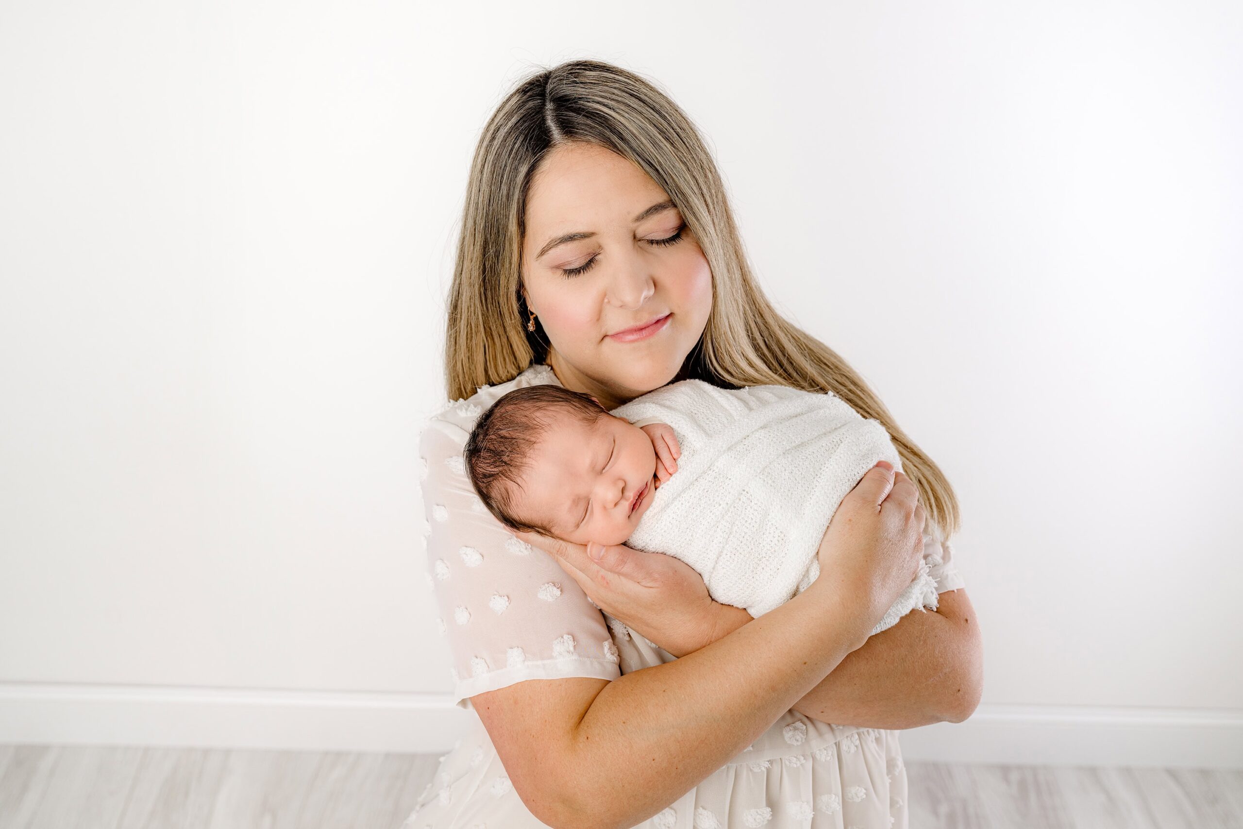 mom cradles her newborn son wrapped in white during his infant photos