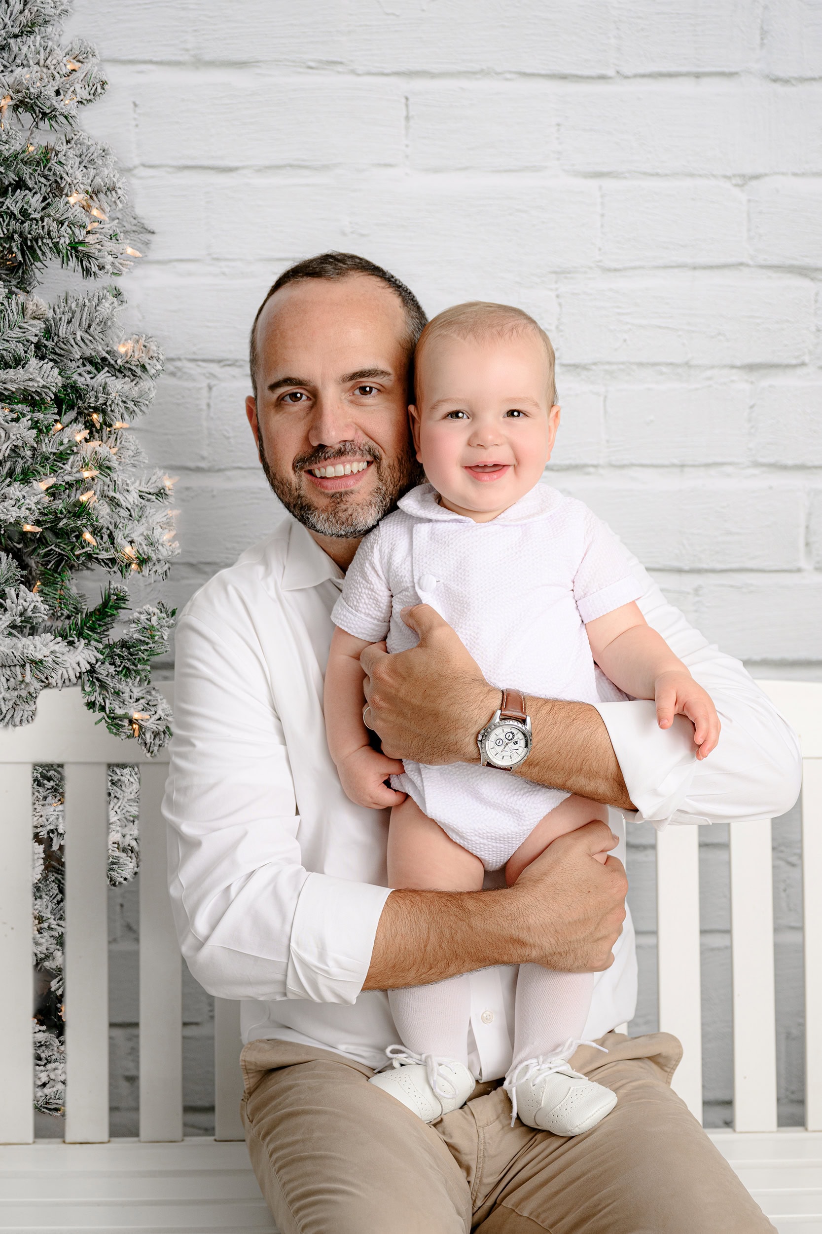 dad cuddles his son smiling in a studio white christmas tree holiday mini session