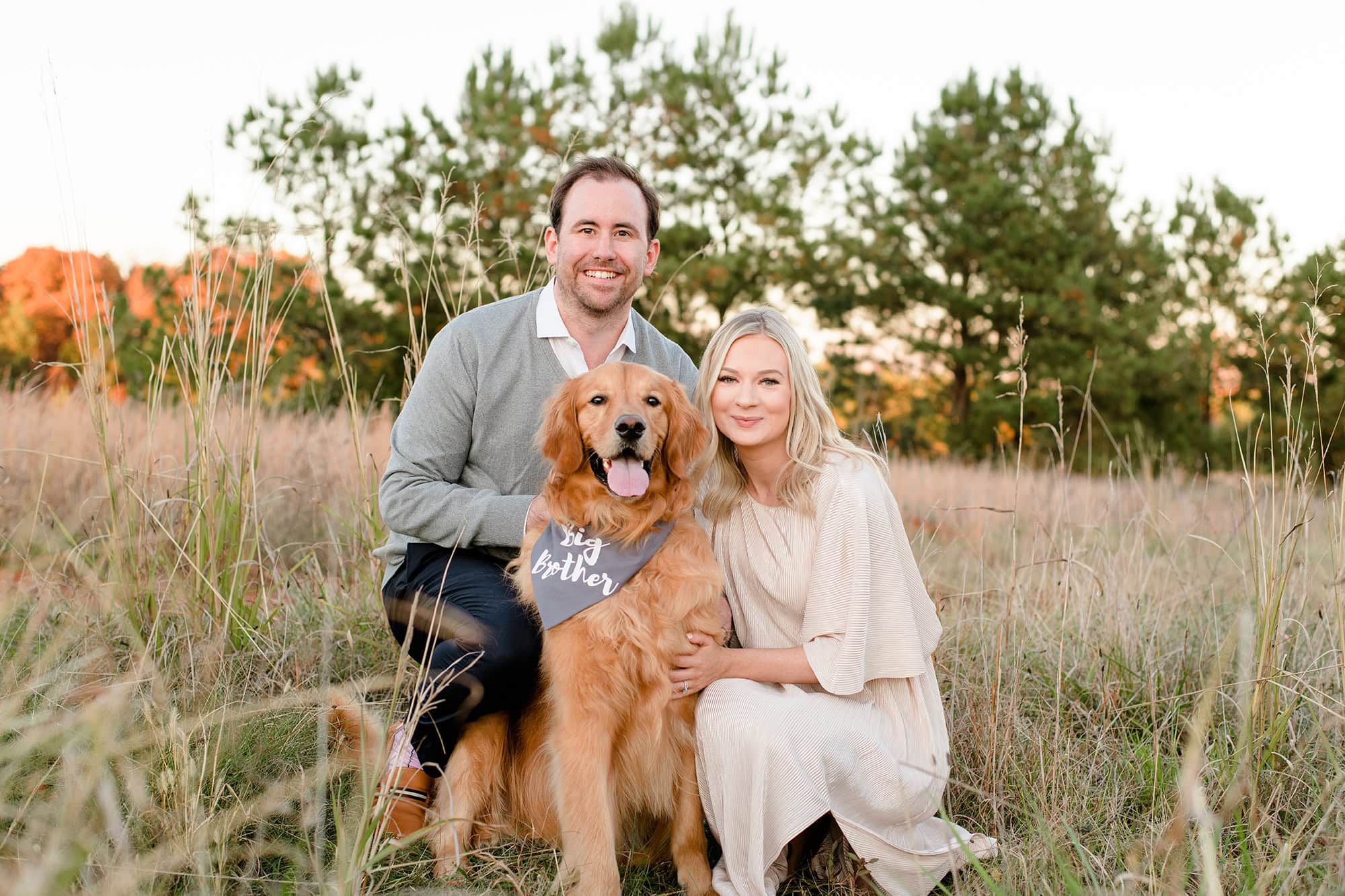 couple squatting in a field with their dog wearing a "big brother" scarf for their gender reveal