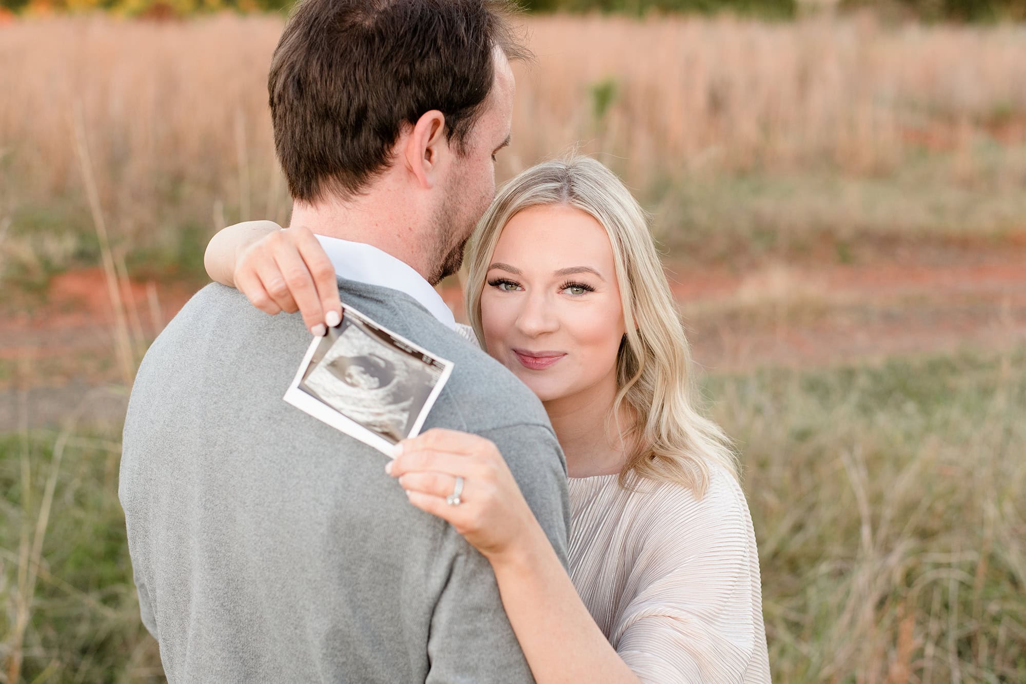 expectant mother holds ultrasound photo over dad's shoulders