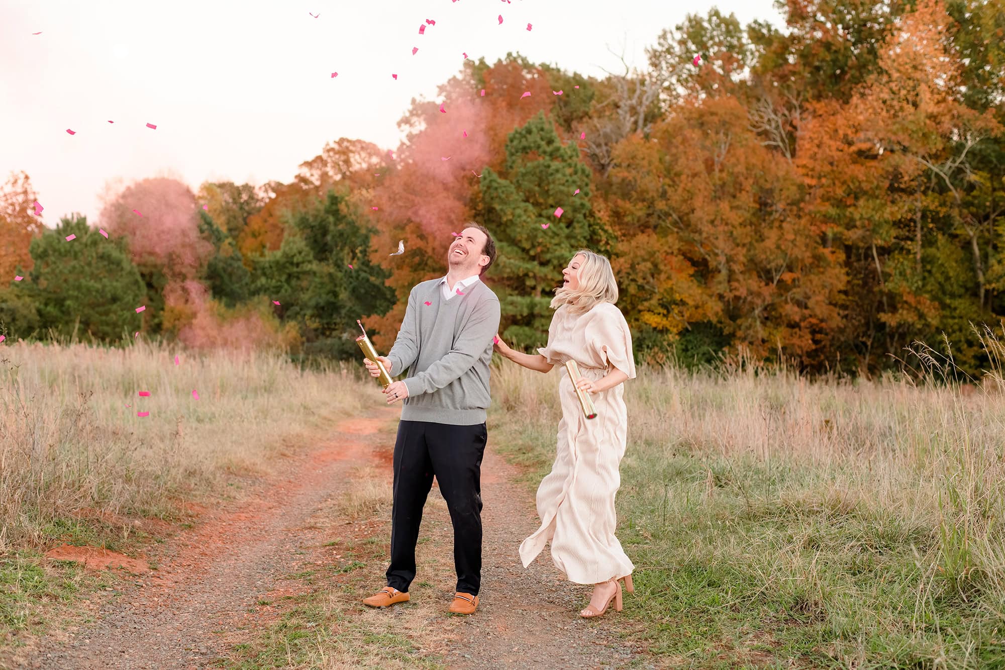 dad twisting confetti and smoke cannon as expectant mom jumps in excitement at gender reveal photo session