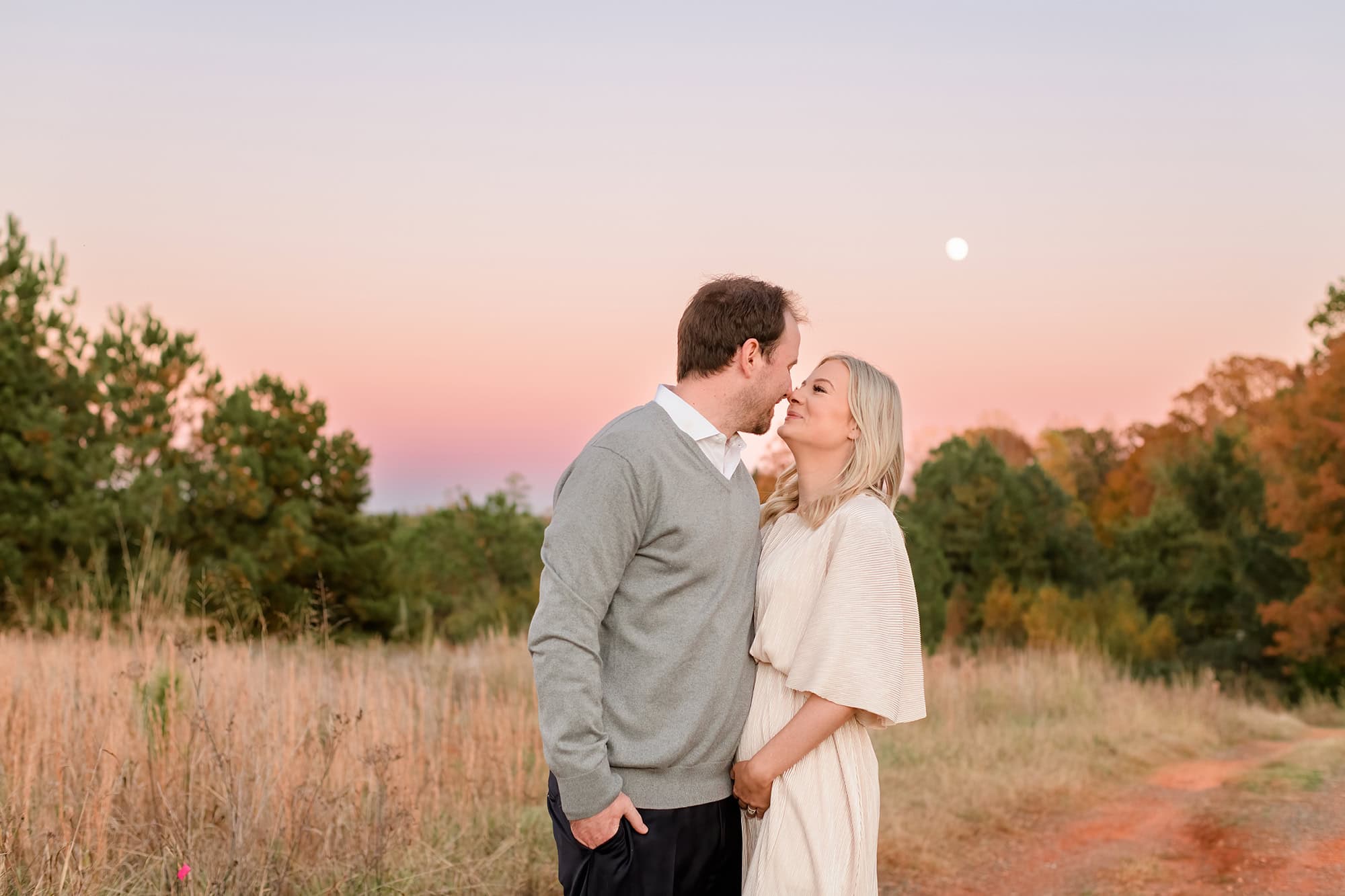 expectant couple celebrates gender reveal with pink cotton candy sky behind them