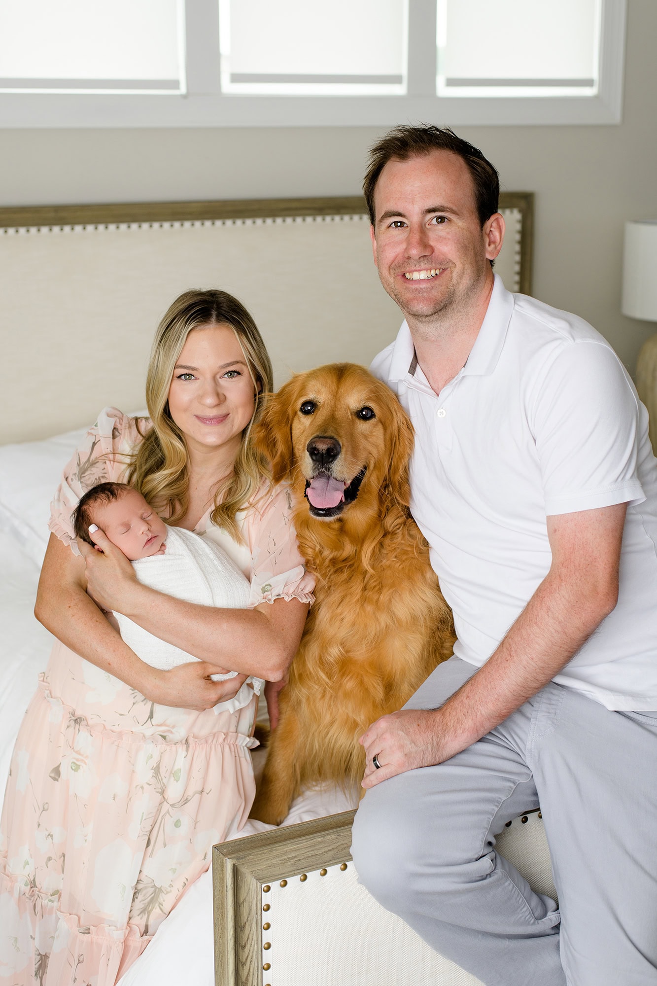mom holds newborn daughter and dad sits beside them with dog in the middle during their in home newborn session