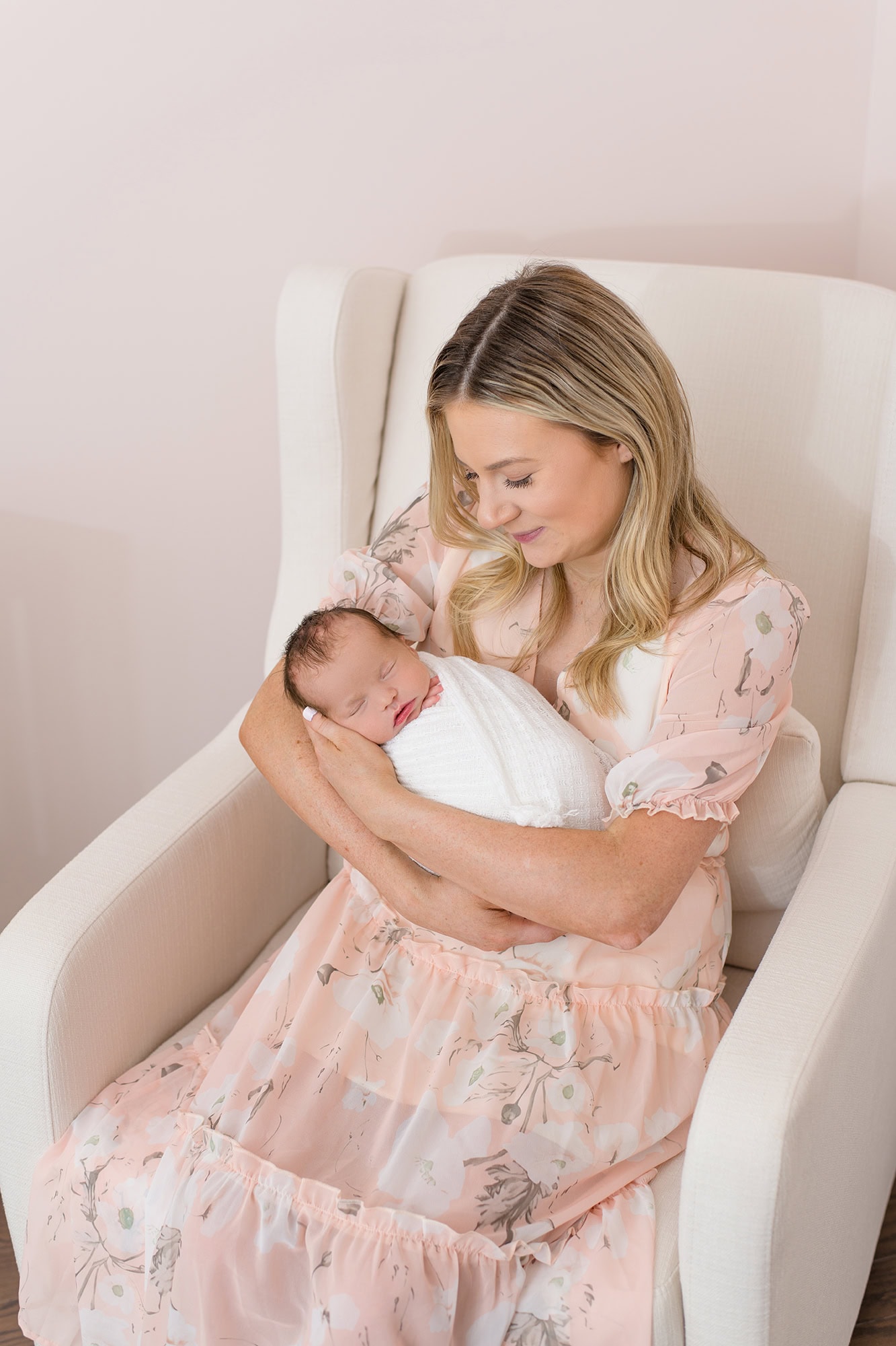 mother looking down at newborn daughter during their lifestyle newborn session in their baby nursery 