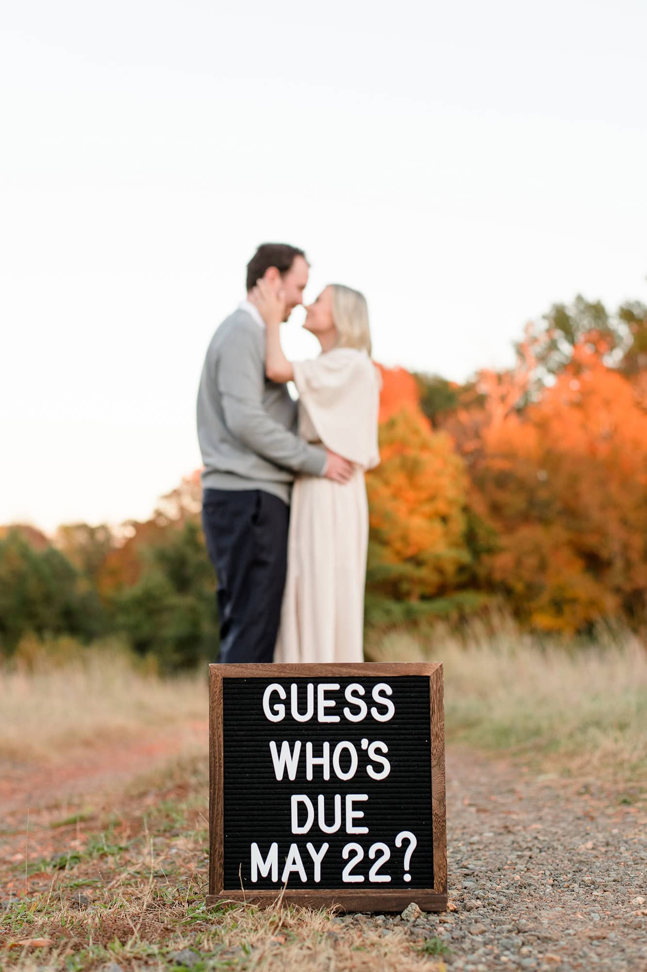 a fun guess who's due sign for a gender and pregnancy announcement with expectant couple standing in background