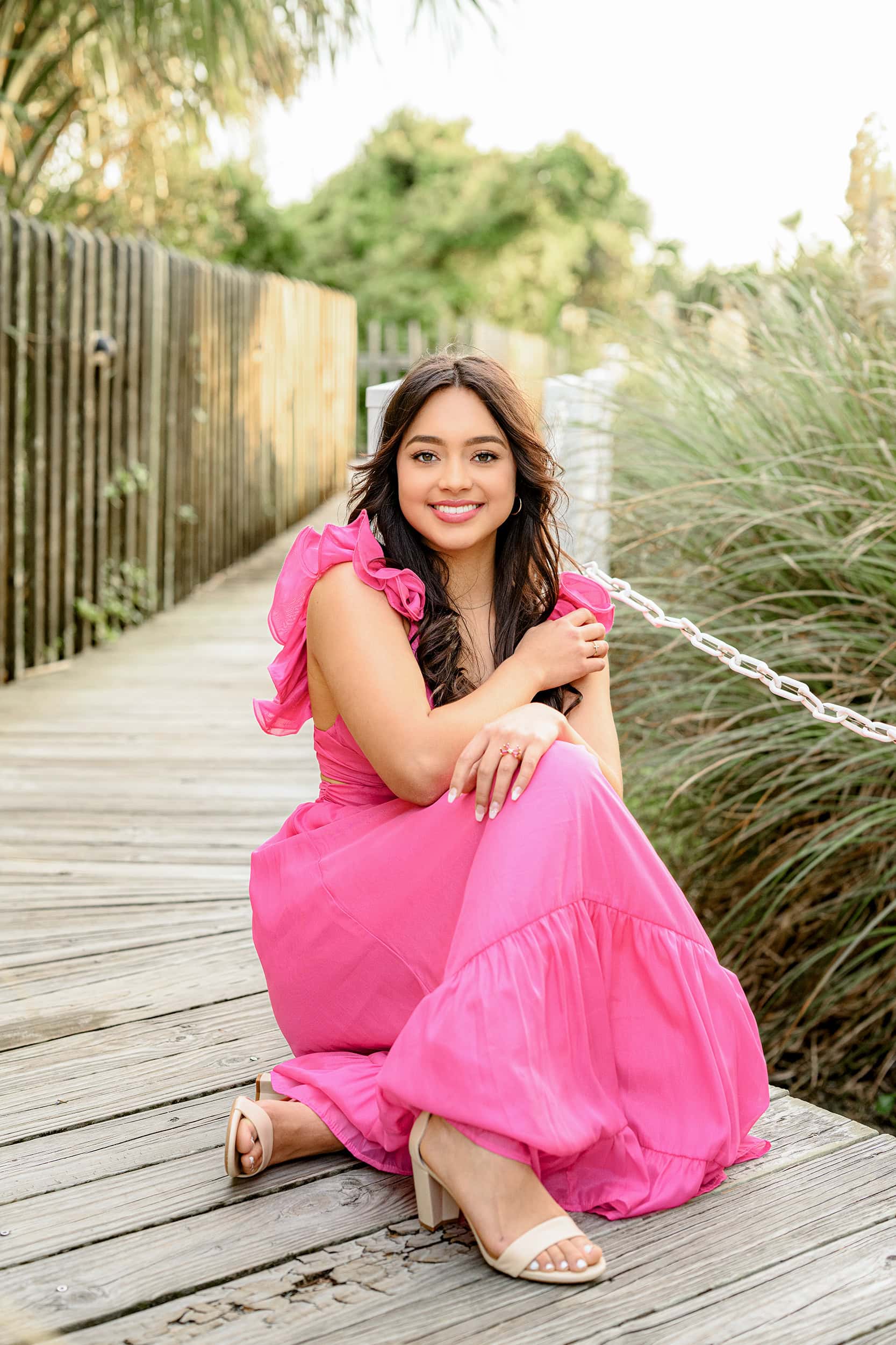 bright pink dress with decorative sleeve is from store iris and poppy for this seniors graduate photos in charleston sc