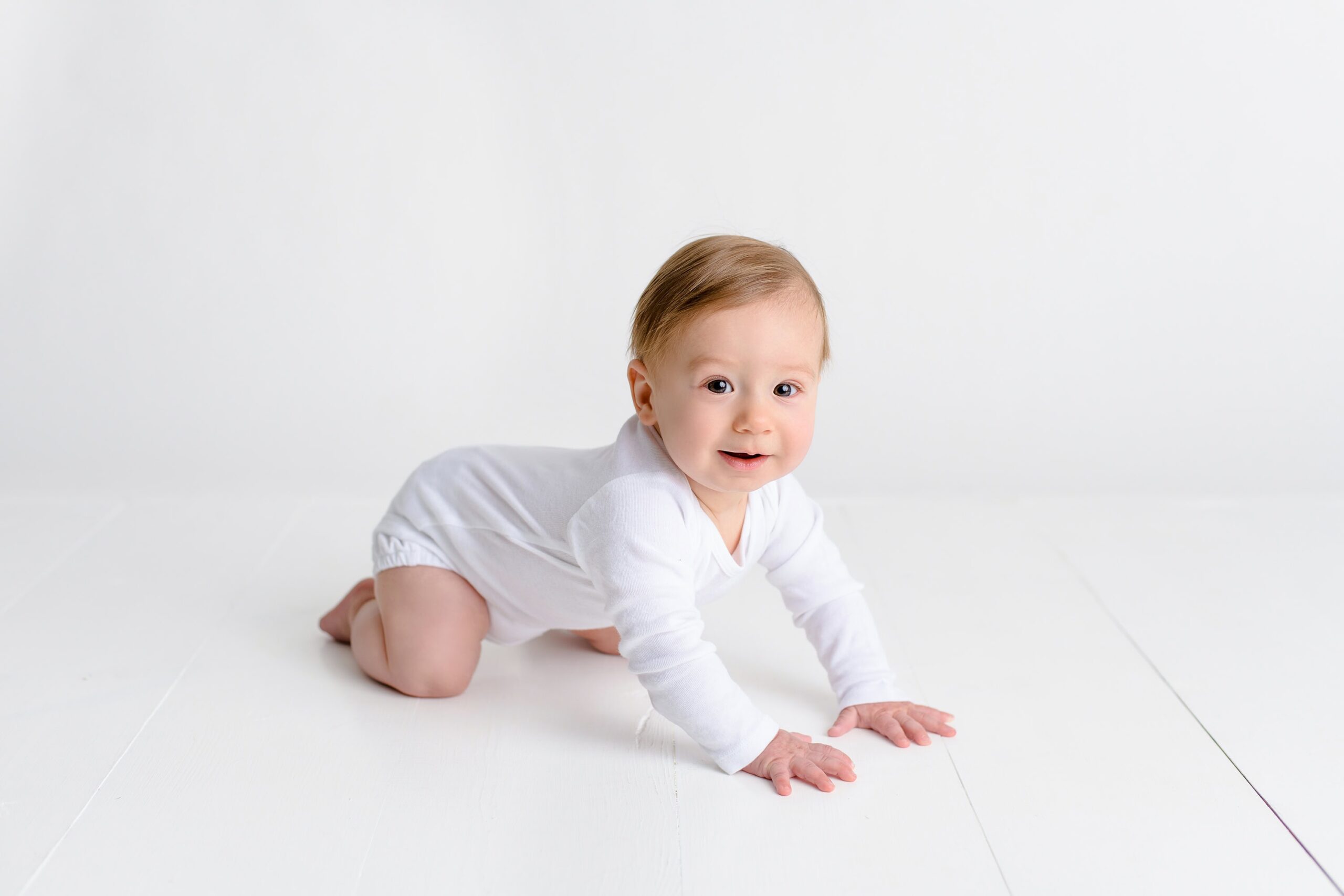 little boy sits up on his knees during his 7 month old sitter session wearing a white long sleeve shirt