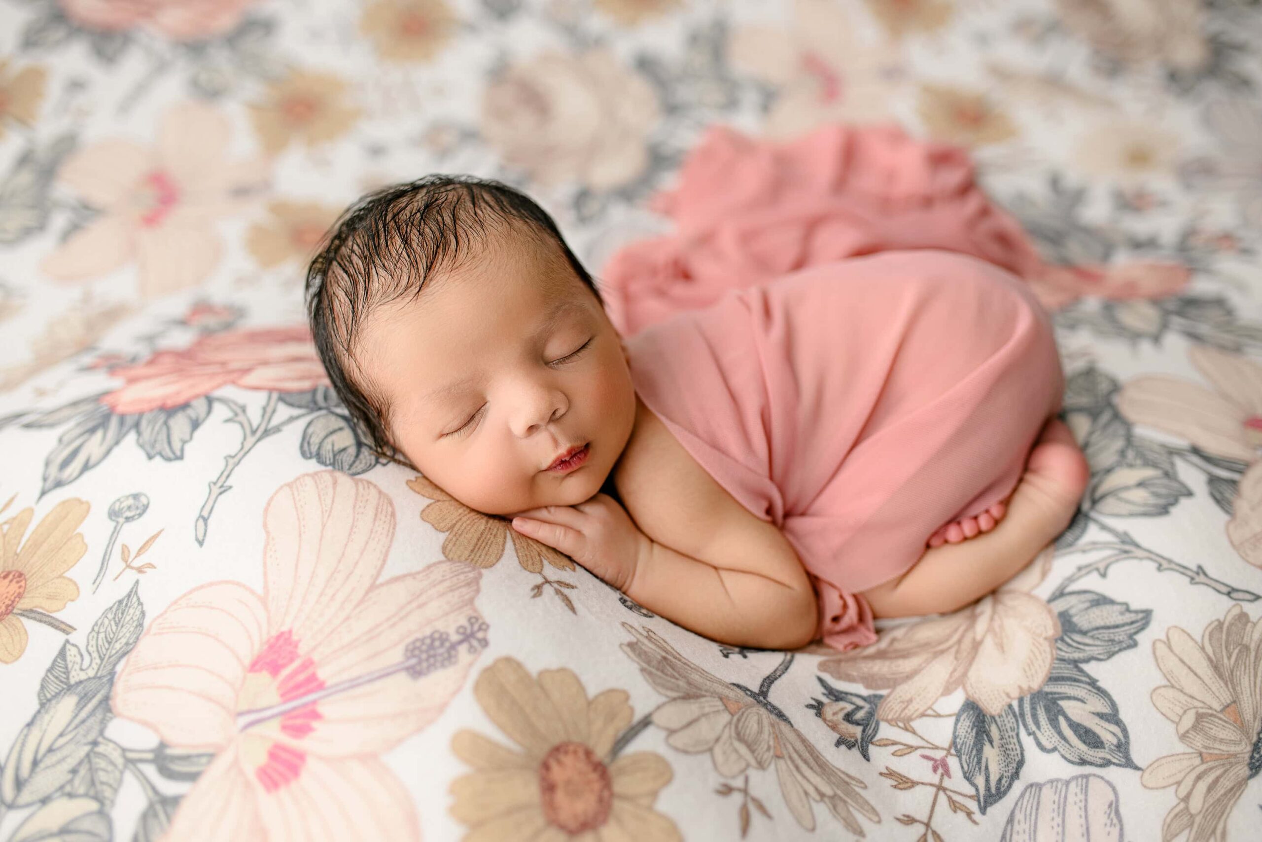 Newborn girl posed laying on her belly with her hand under her cheek on a floral background to match her nursery decorations