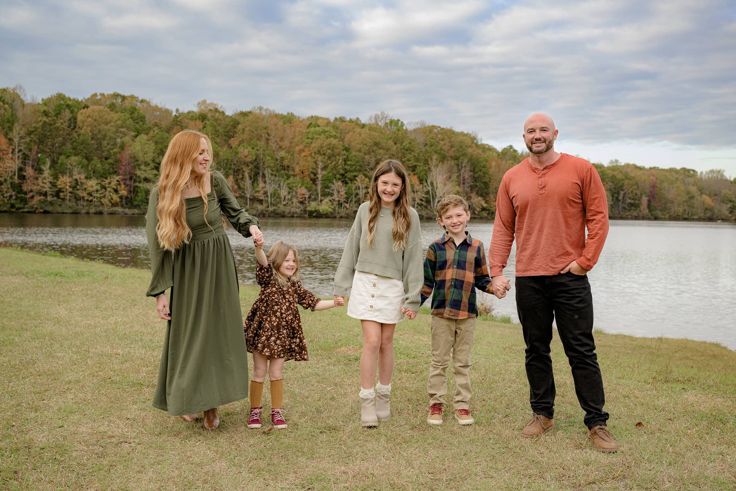 family of five stands in front of a lake in prime fall season dressed in fall tones
