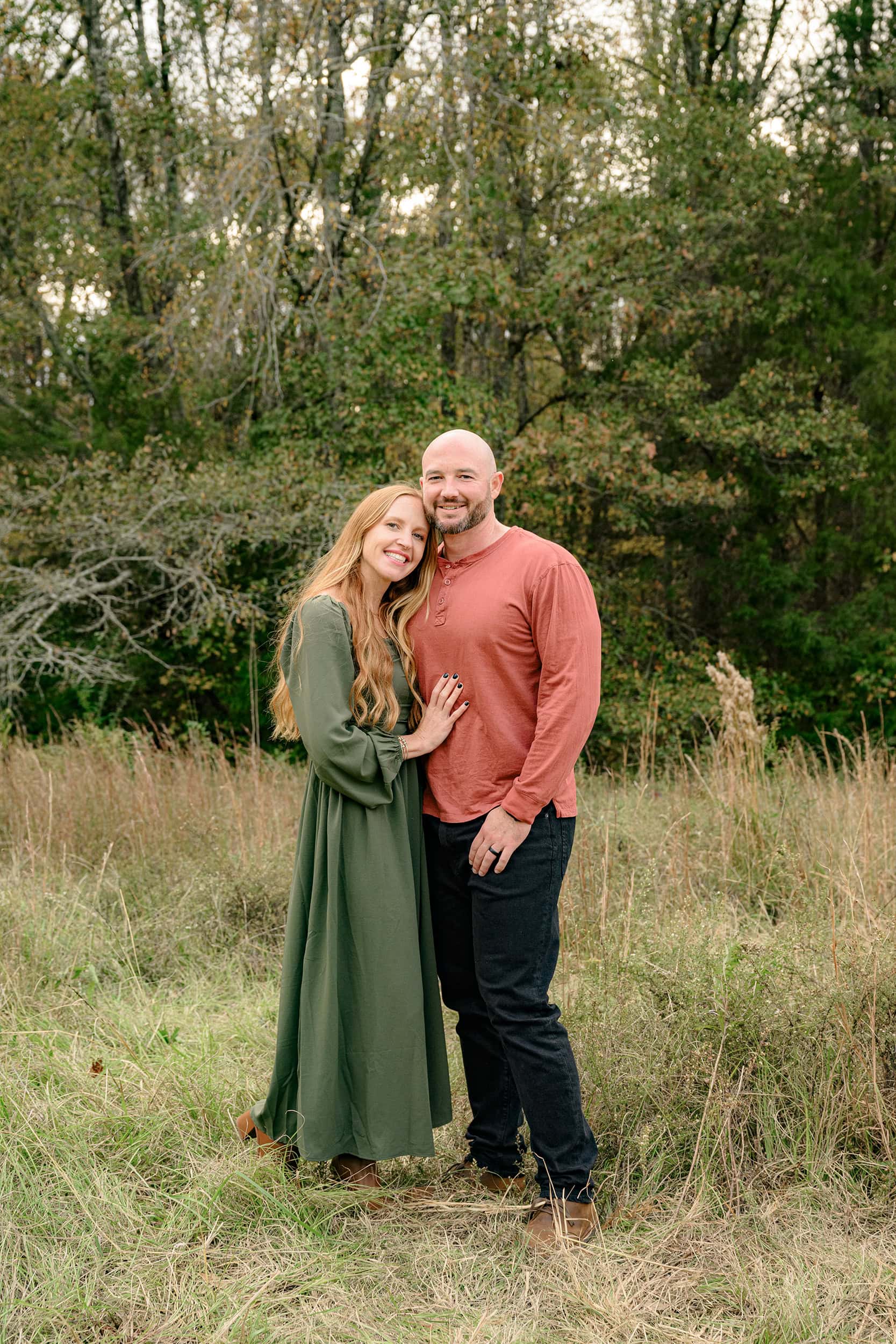 red headed woman dressed in green hugs her husband dressed in rust in peak fall colors in a waxhaw area park