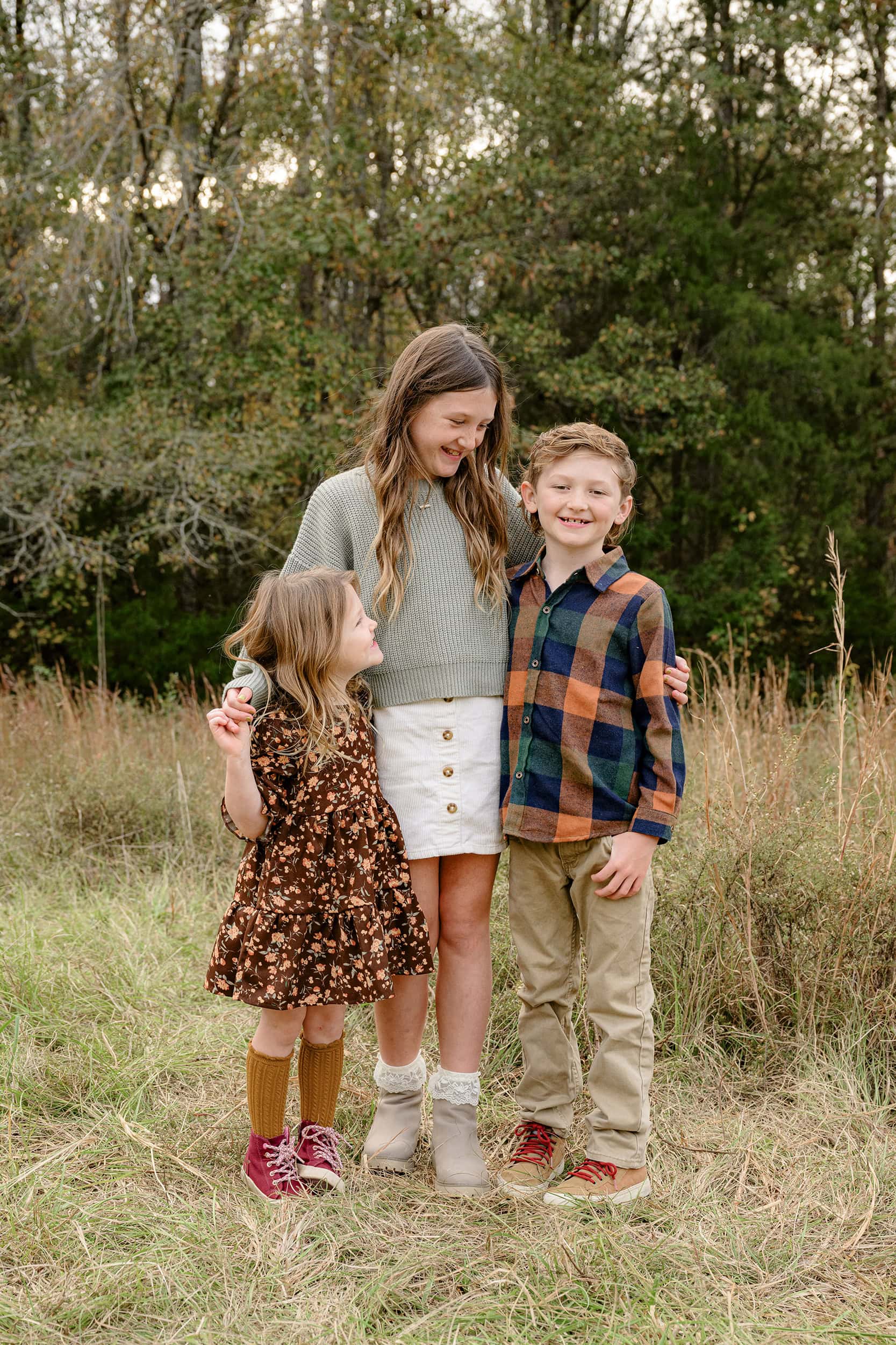 three siblings dressed in fall colors standing in a charlotte area field in peak fall season