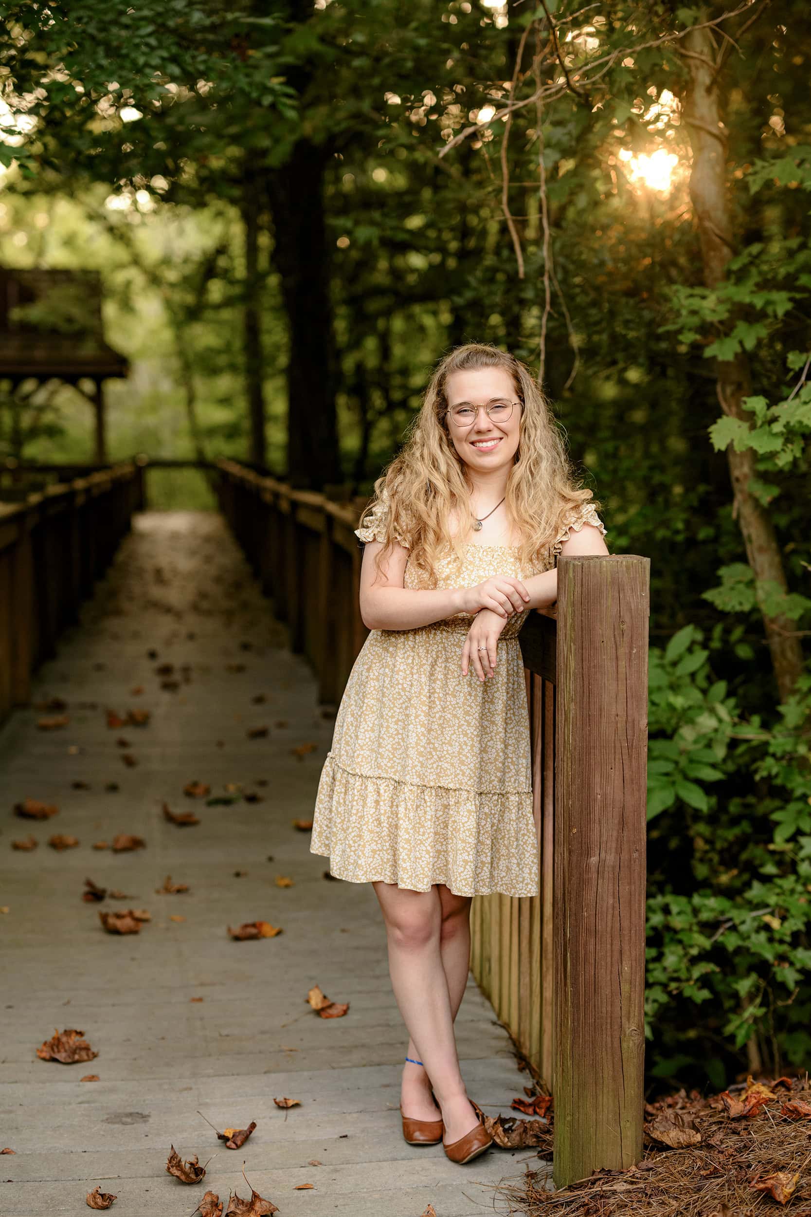 charlotte senior portrait of a graduate standing against a wooden railing in peak fall tones behind her